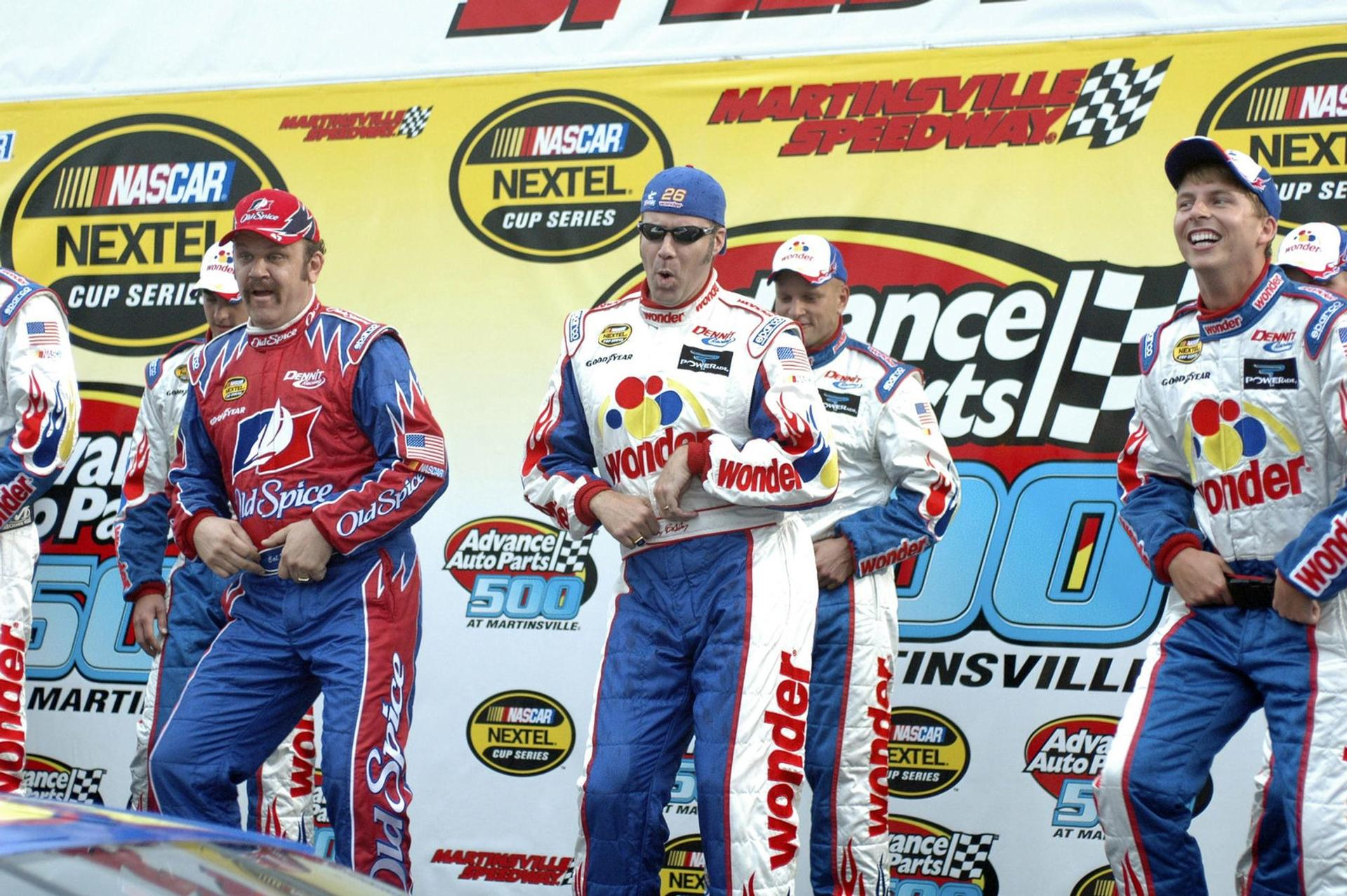 Rennfahrer in farbenfrohen Overalls tanzen vor einer Kulisse mit Logos von NASCAR und Martinsville Speedway.