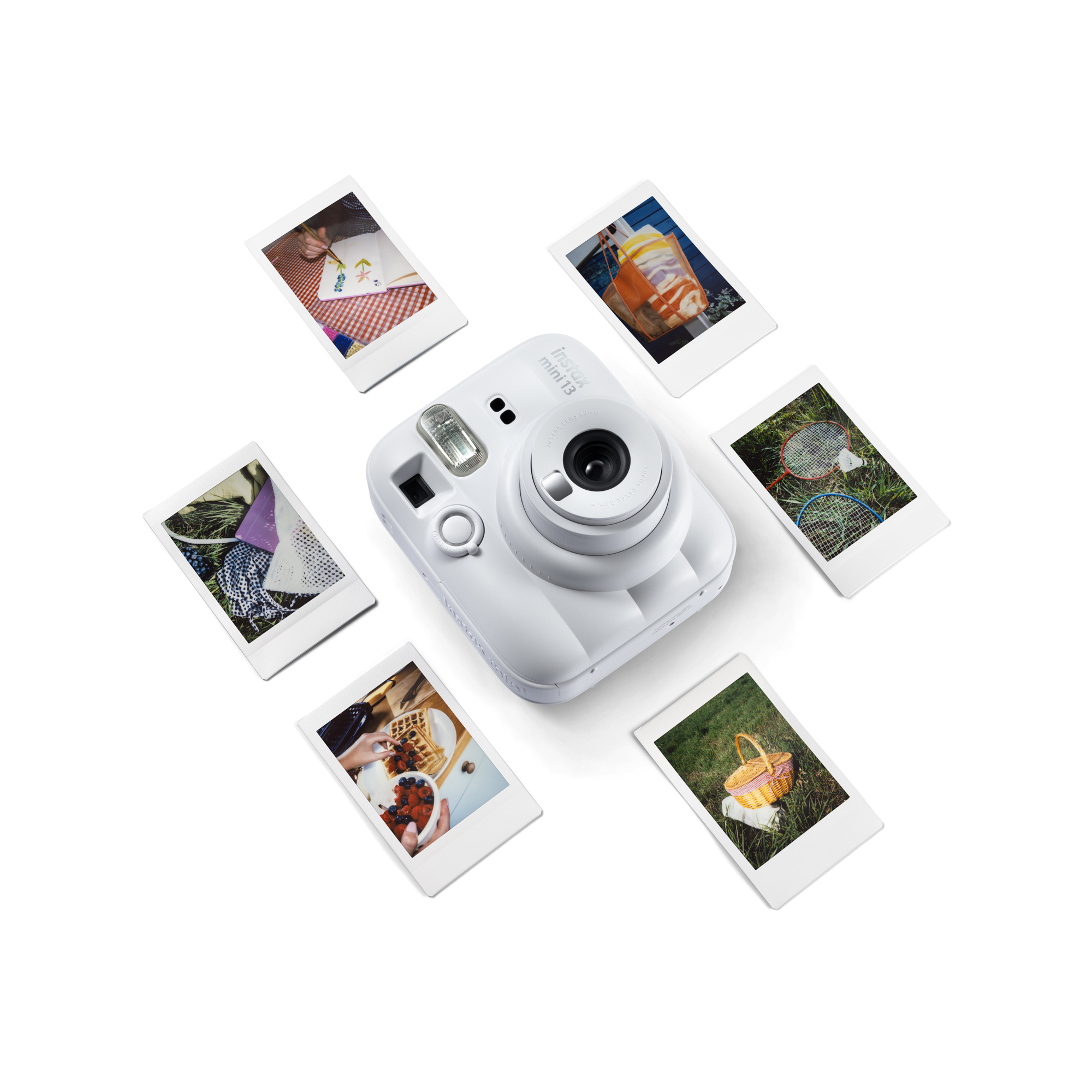 Egy fehér Instax Mini 13 kamera piknik, játék és étel fotóival körülvéve.
