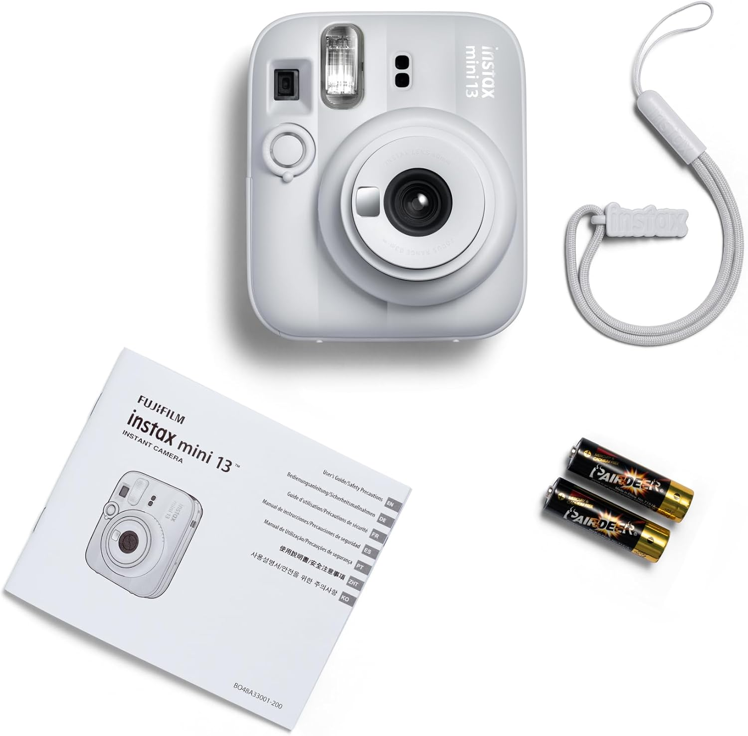 Fehér Instax Mini 13 kamera kézikönyvvel, csuklópánttal és két elemmel.
