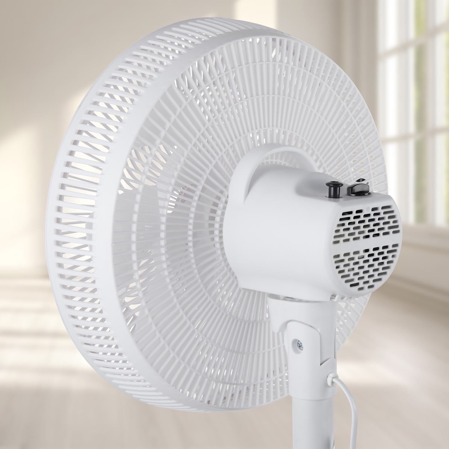Un ventilateur sur pied blanc vu de dos avec une fenêtre ouverte en arrière-plan.