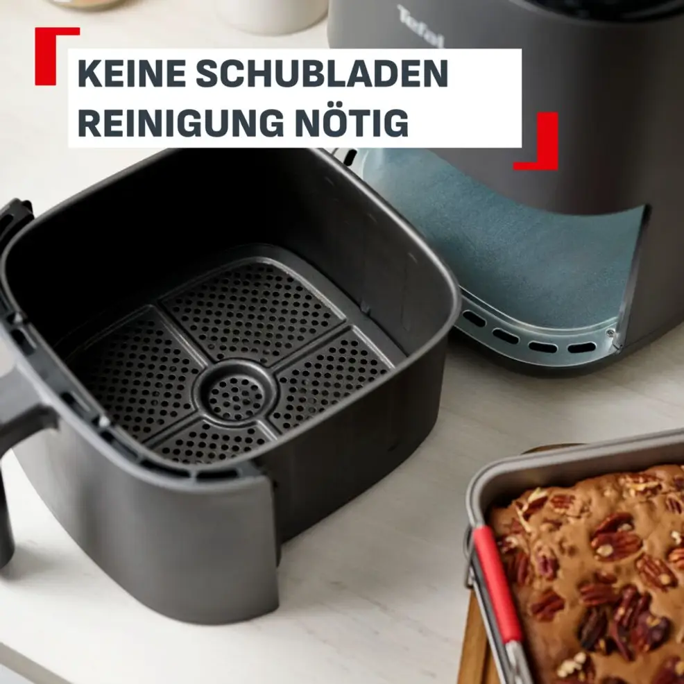 Une friteuse à air noire avec son panier retiré, à côté d'un gâteau aux noix.