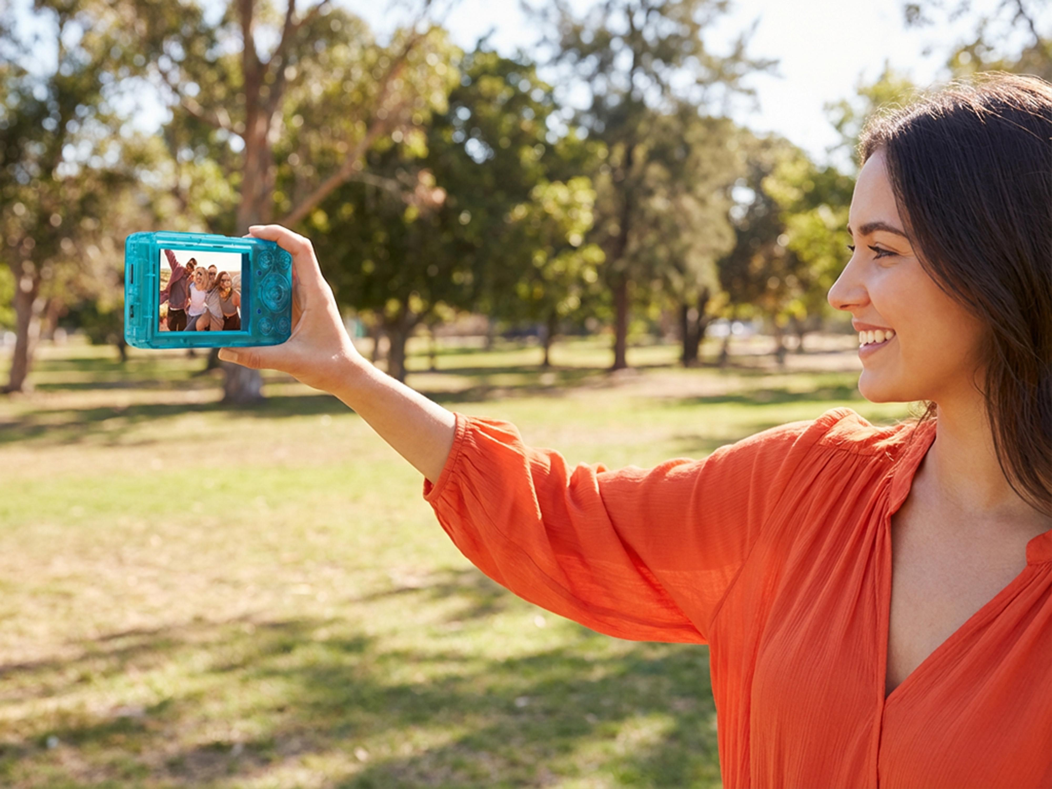 Frau macht ein Selfie mit Freunden im Park auf einem hellblauen Digitalkamera.