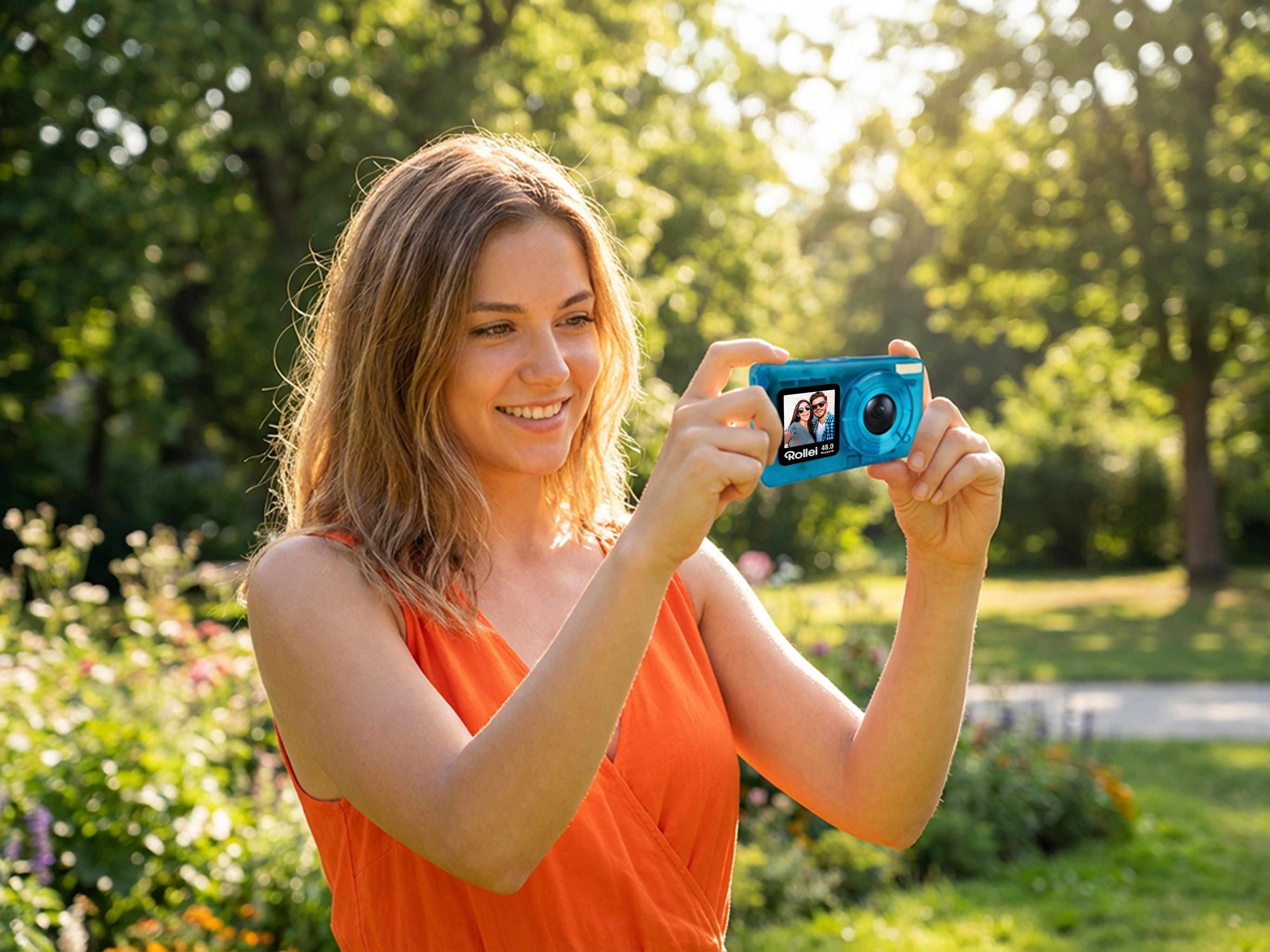 Eine Frau in einem orangen Kleid fotografiert mit einer blauen Kamera im Park.