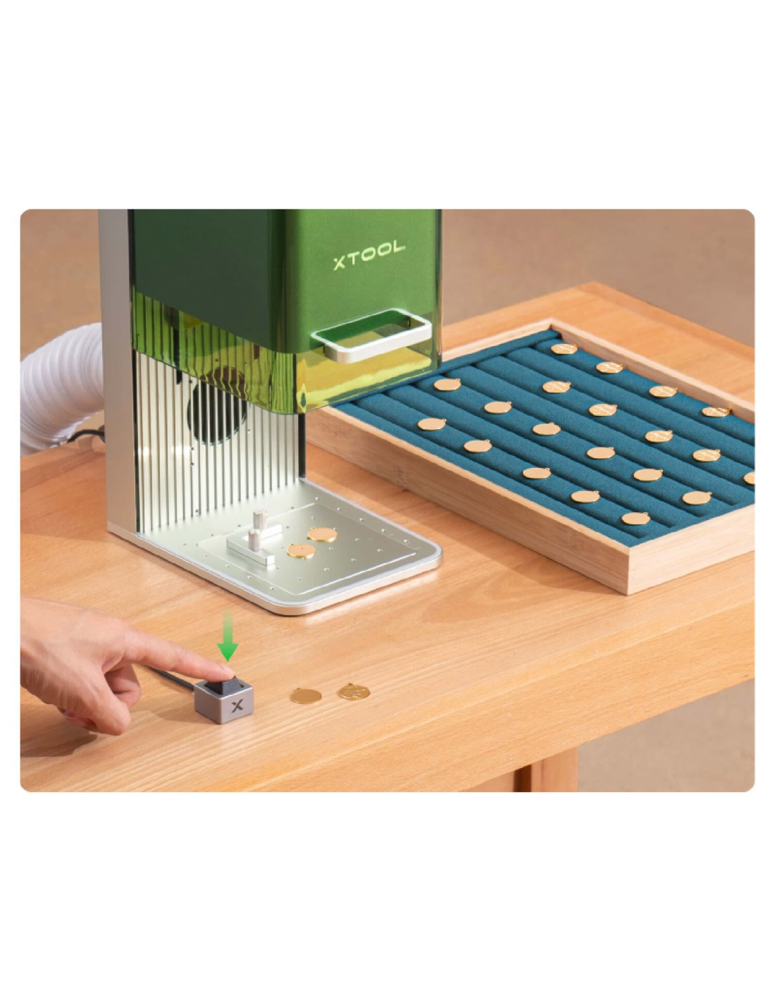 Un dispositivo XTOOL verde sobre una mesa de madera grabando pequeños objetos dorados.