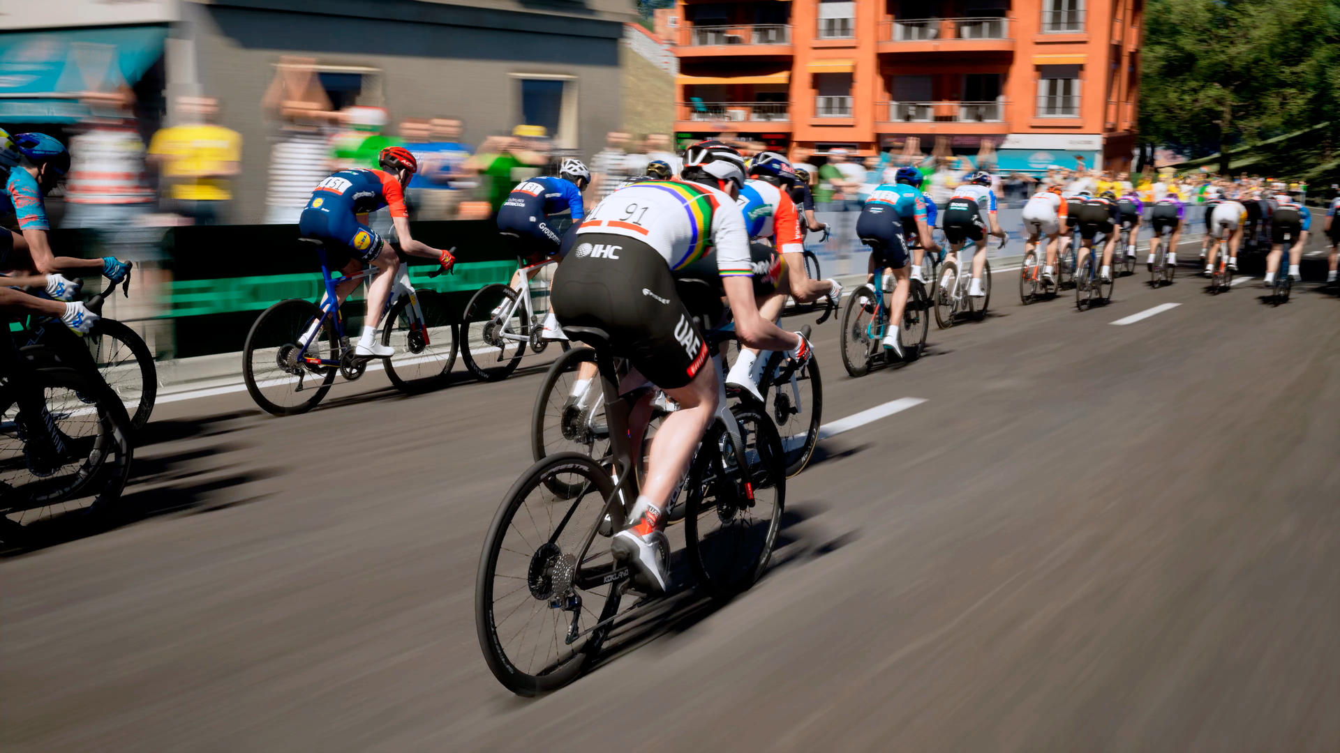 Radsportler fahren in einer Gruppe auf einer Straße mit Gebäuden und Zuschauern im Hintergrund.