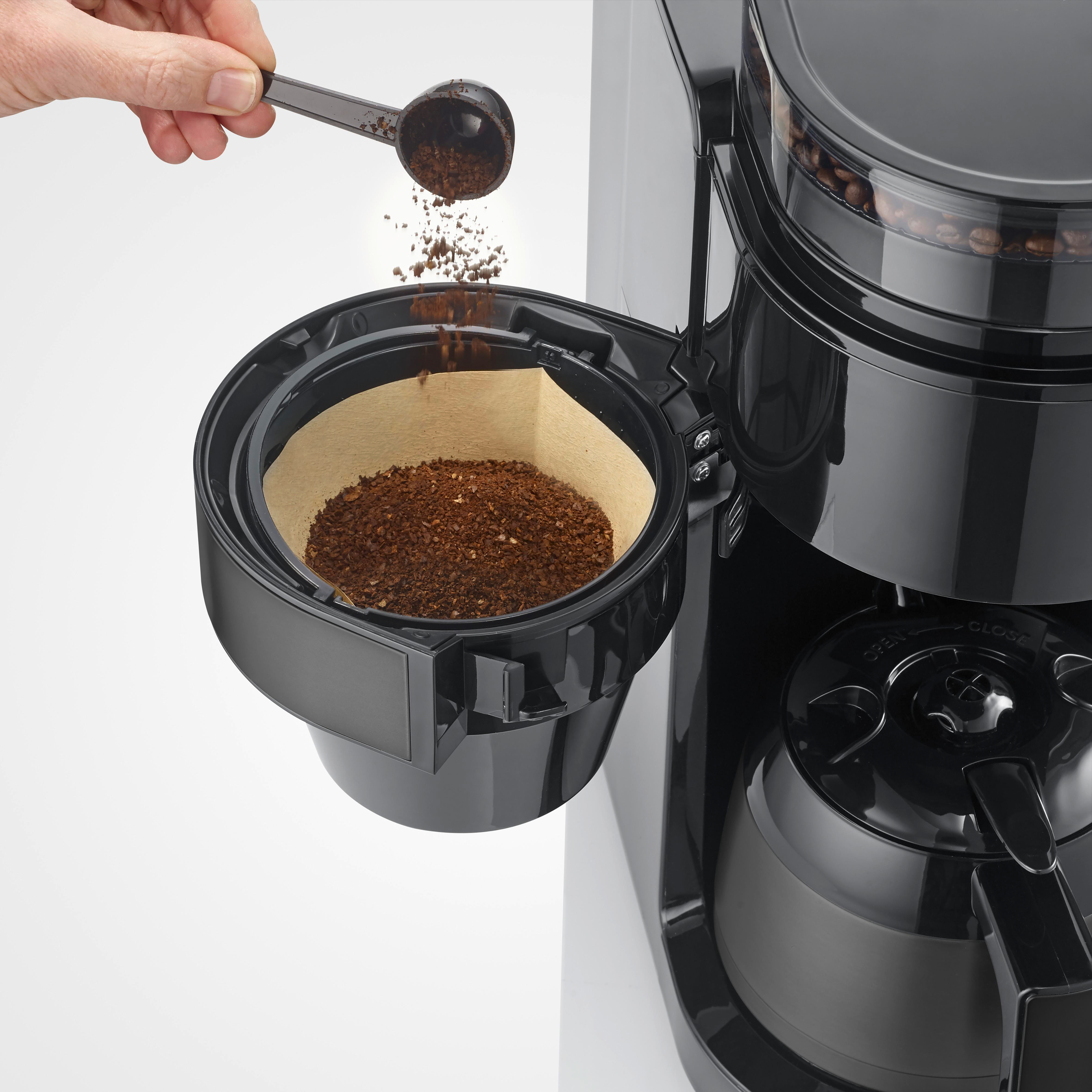Eine Hand gibt Kaffeepulver in einen Kaffeefilter einer Kaffeemaschine.