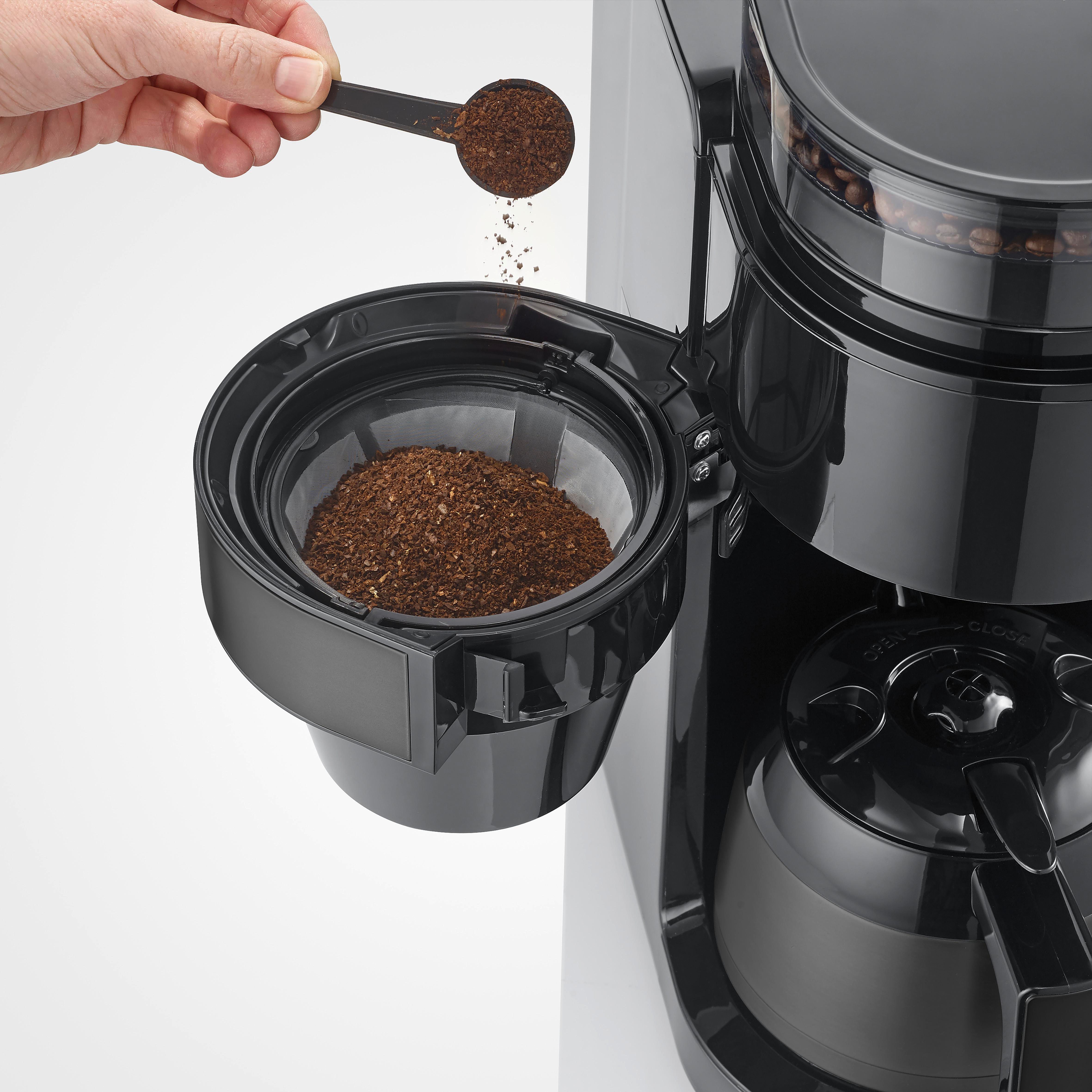 Eine Hand schüttet Kaffeepulver aus einem Löffel in einen Kaffeefilter.