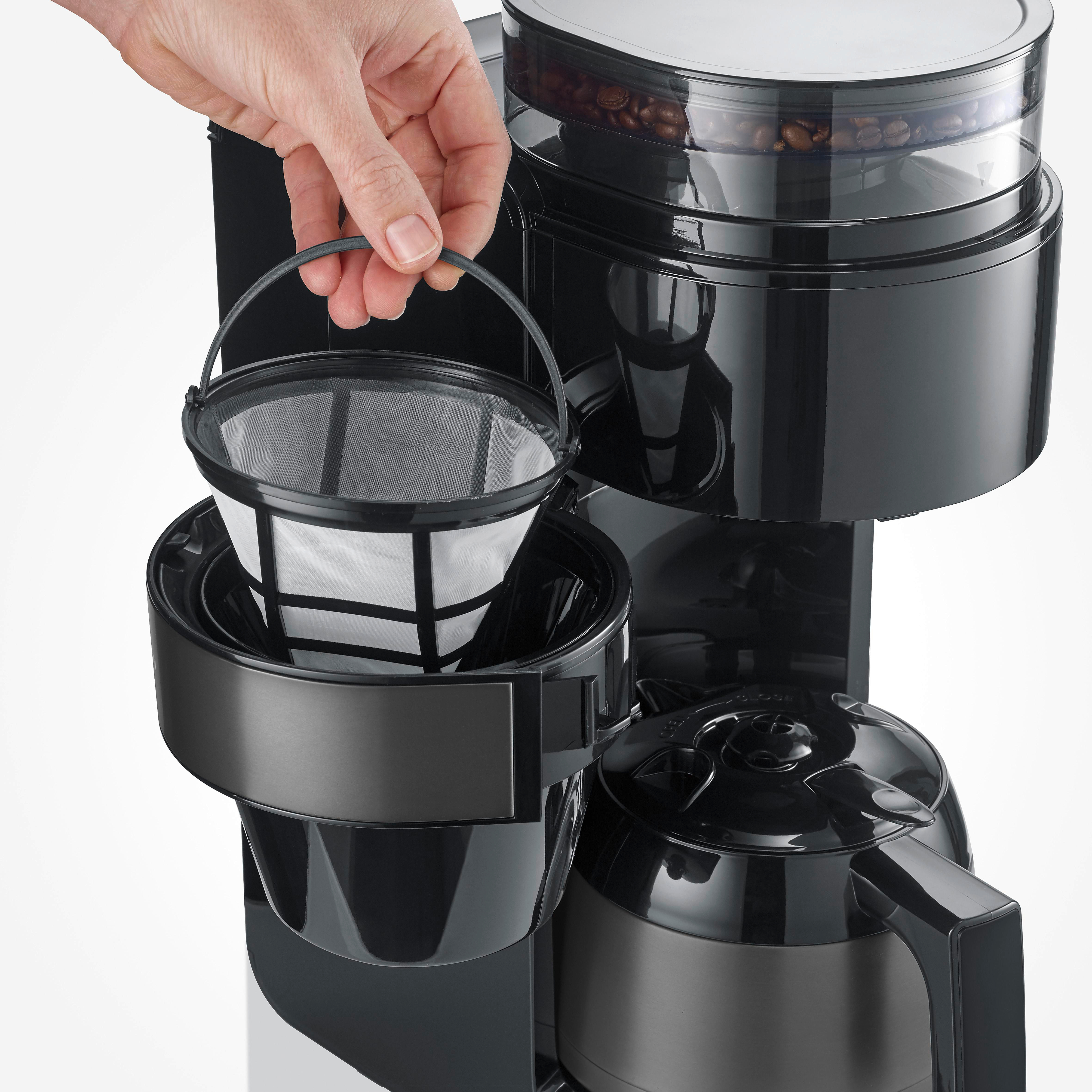 Eine Hand setzt einen weißen Kaffeefilter in eine schwarze Kaffeemaschine ein.