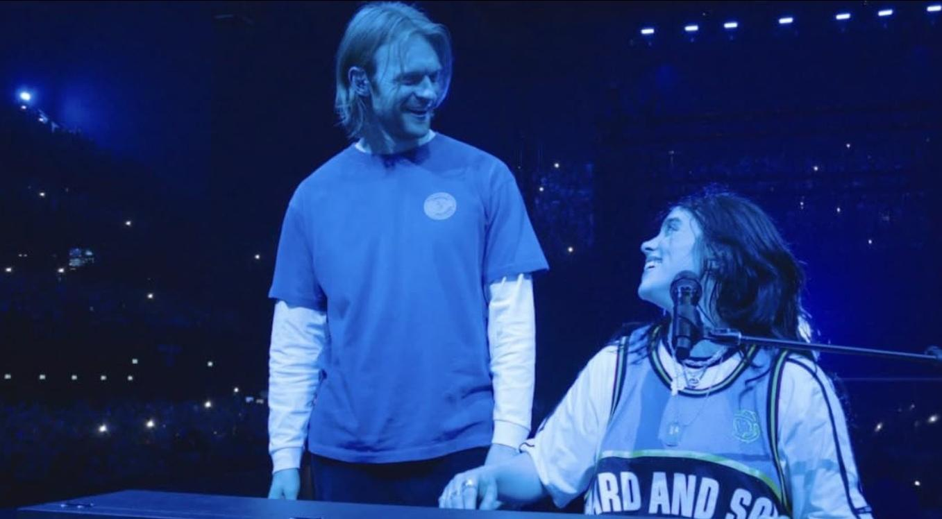 Ein Mann in blauem T-Shirt und eine Frau im Trikot stehen auf der Bühne vor Publikum.