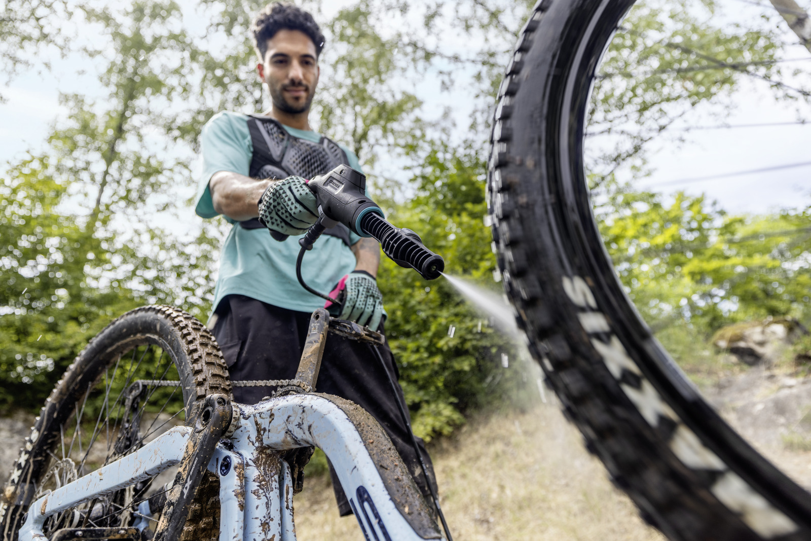 Férfi tisztít sáros mountain bike-ot nagynyomású mosóval a szabadban.