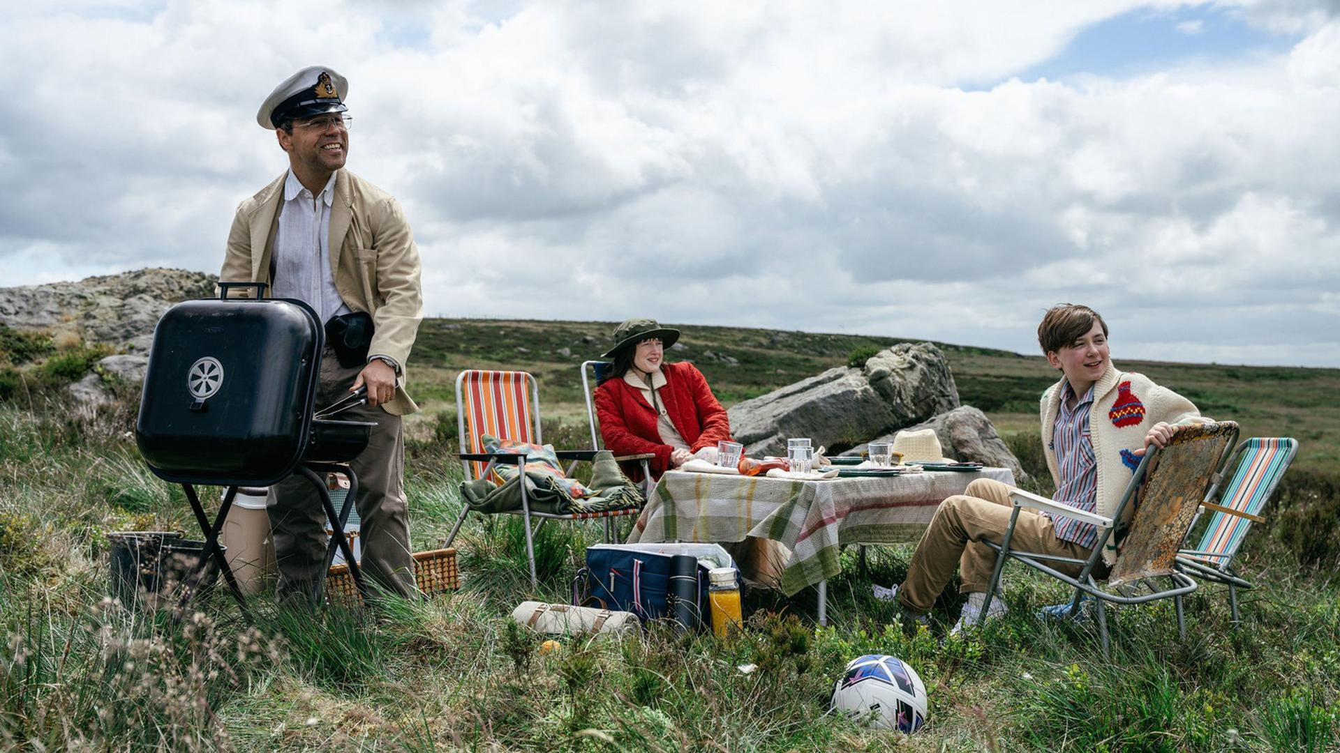 Eine Familie picknickt im Freien mit einem Grill und einem Fußball im Gras.