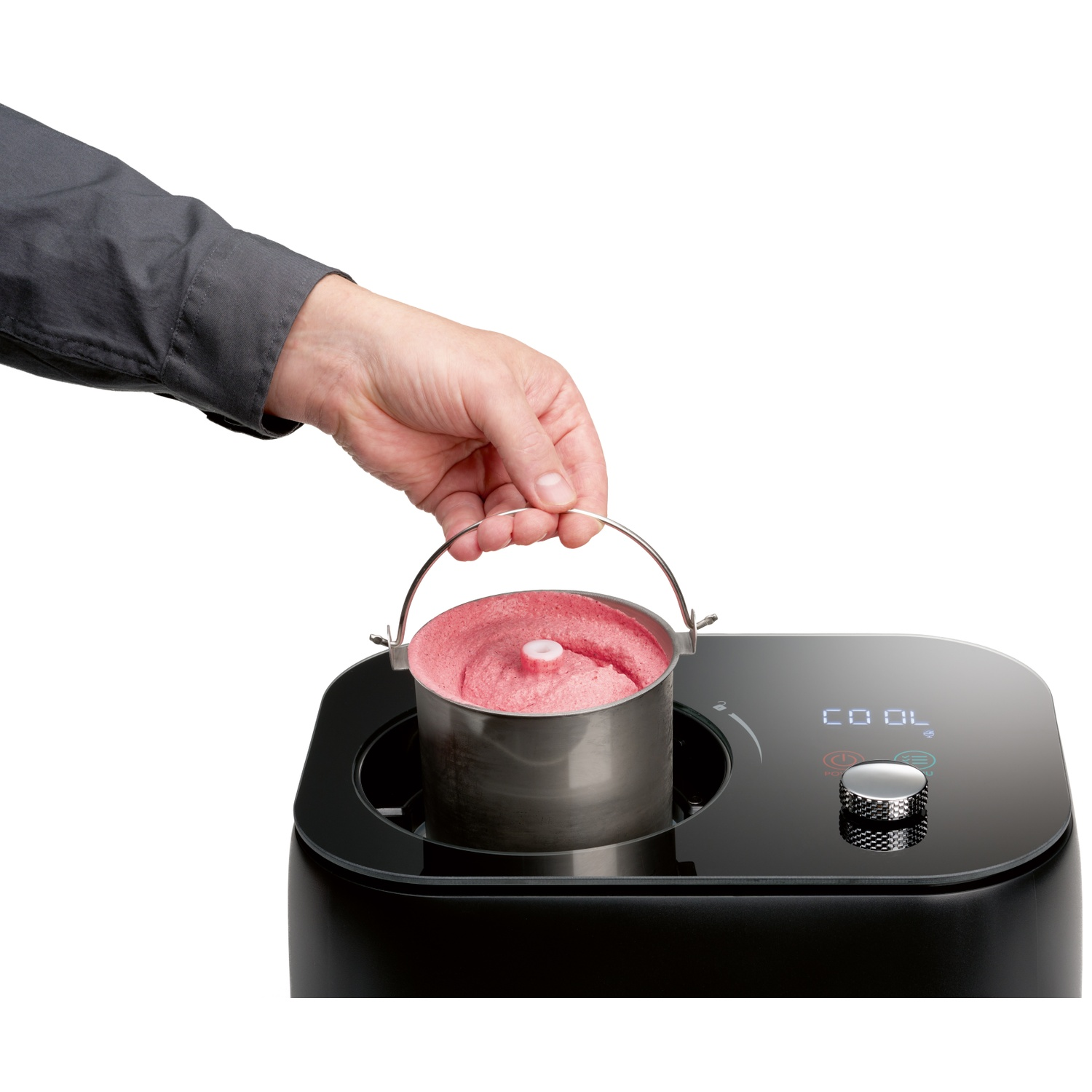 Une main soulève un bol en métal de crème glacée rose d'une sorbetière.