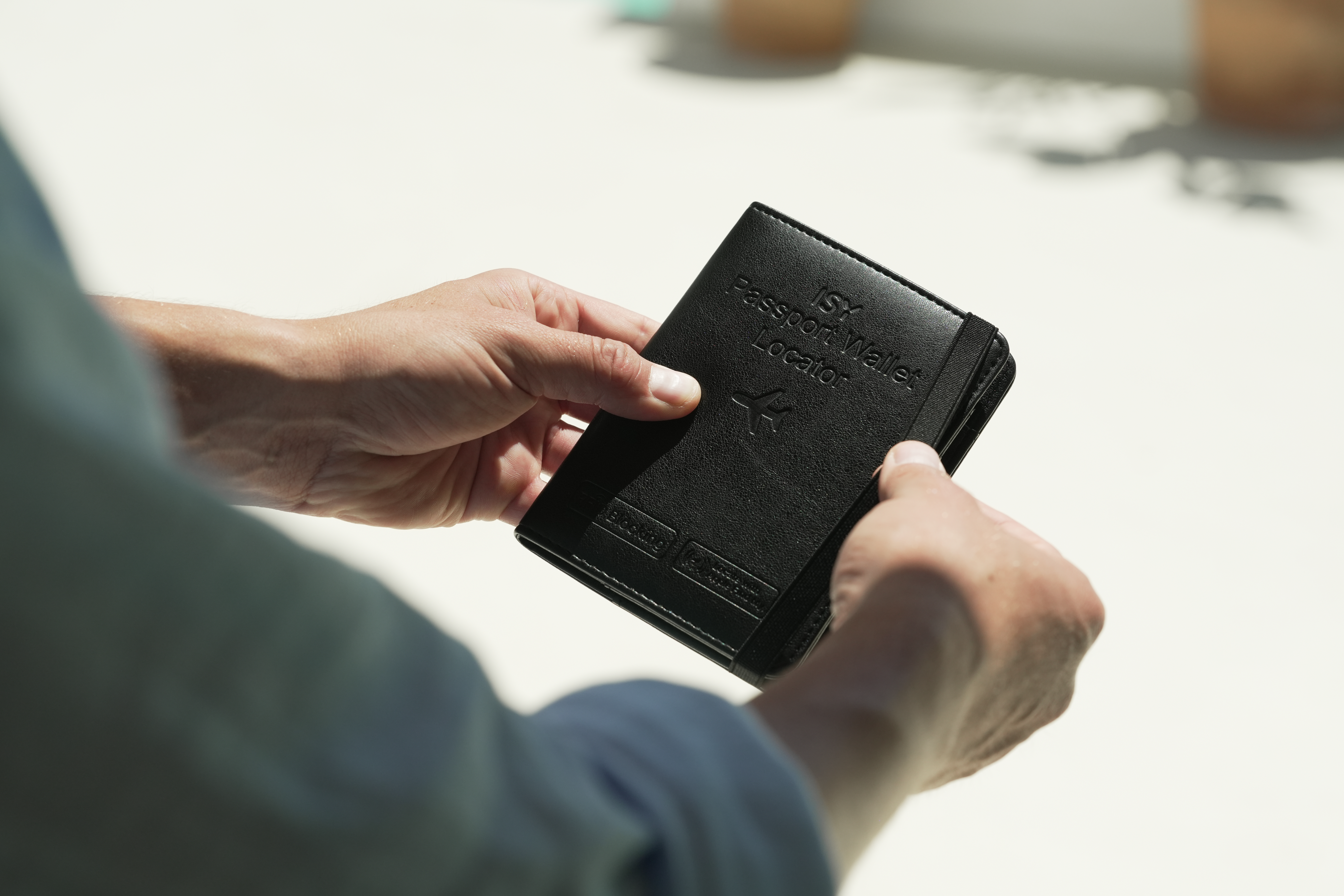 Eine Person hält eine schwarze Reisepassbrieftasche mit der Aufschrift „ISY Passport Wallet Locator“.
