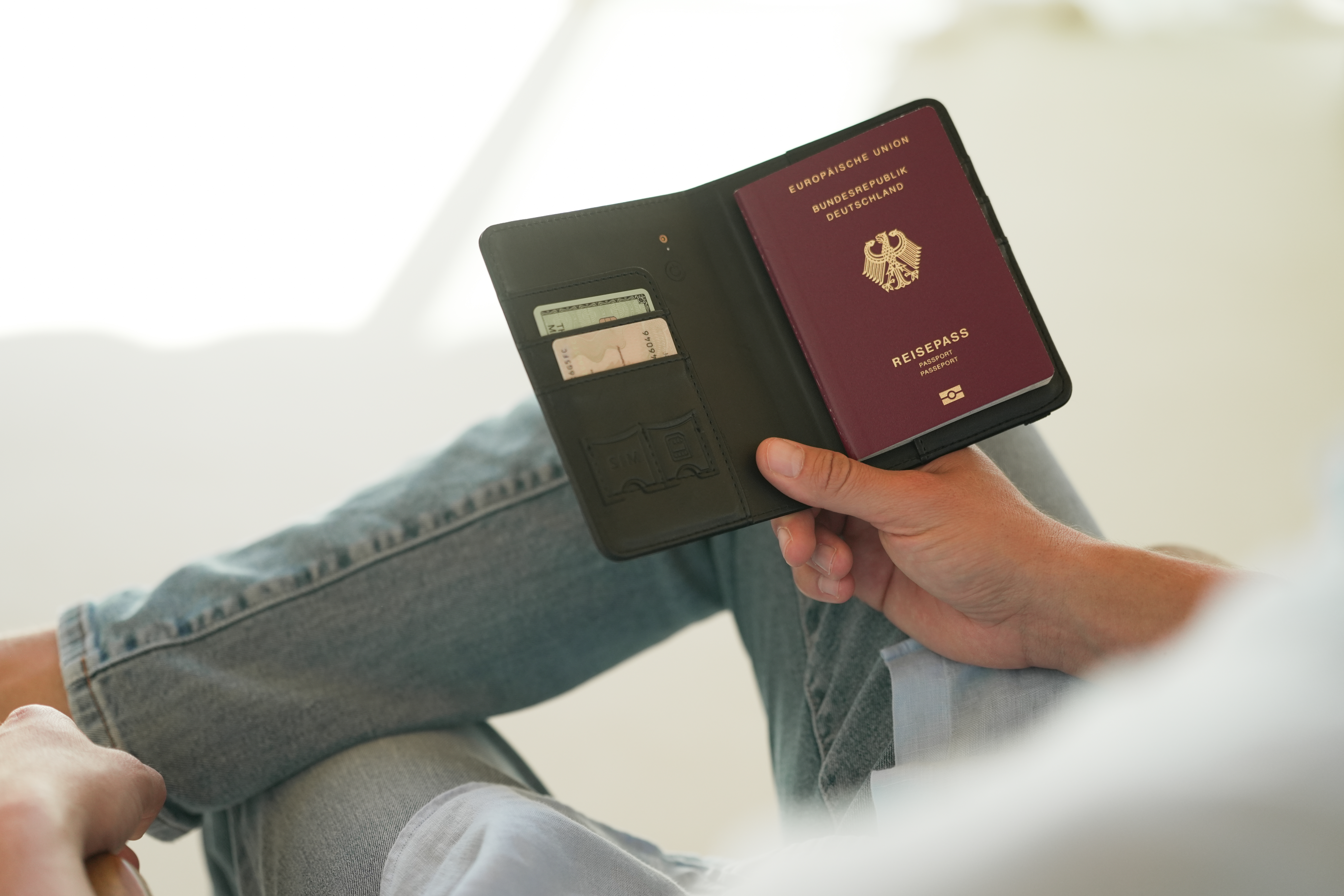 Eine Hand hält einen deutschen Reisepass in einer schwarzen Hülle mit Kartenfächern.