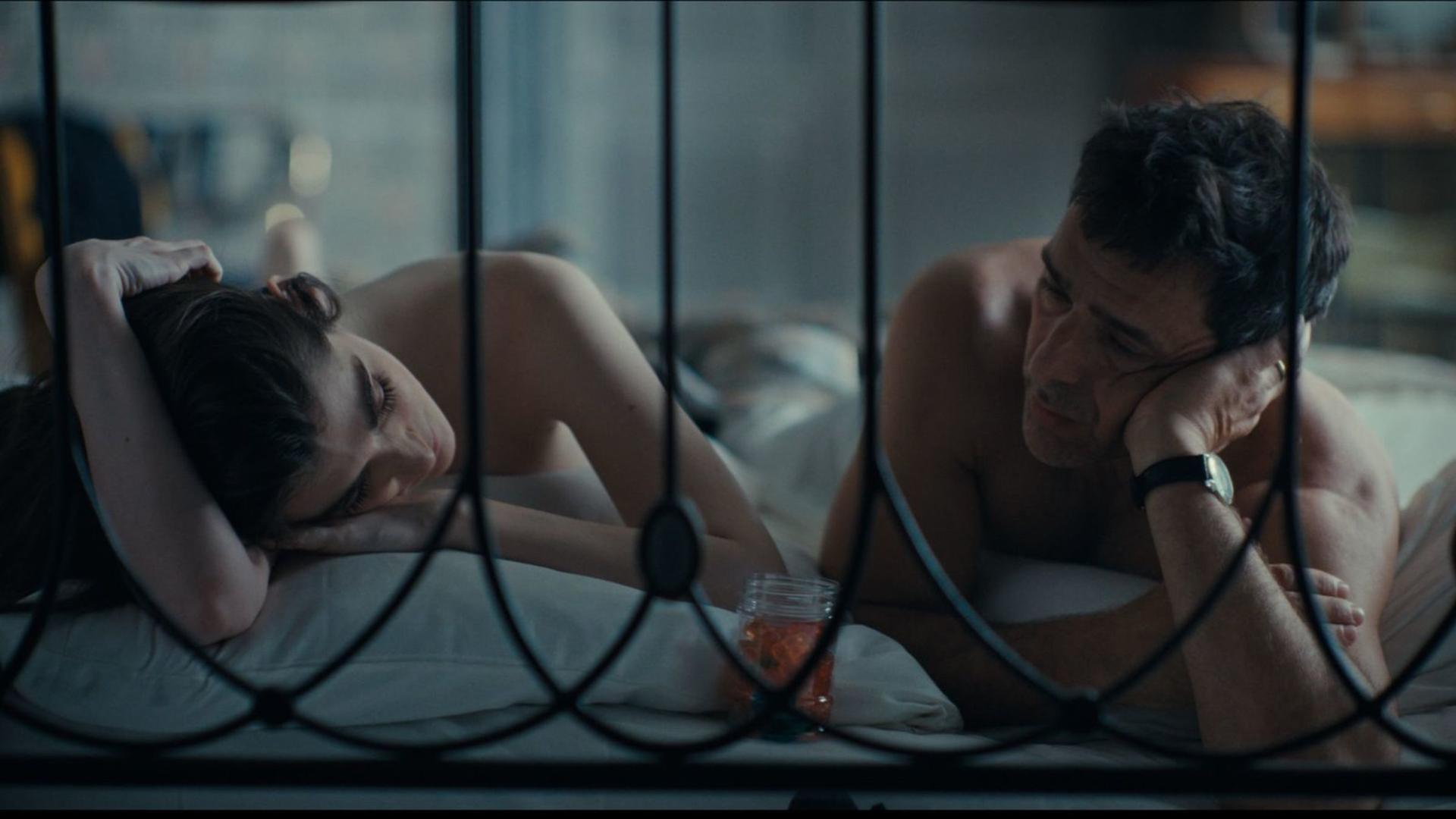 Ein Mann und eine Frau liegen im Bett, durch ein Gitter getrennt.