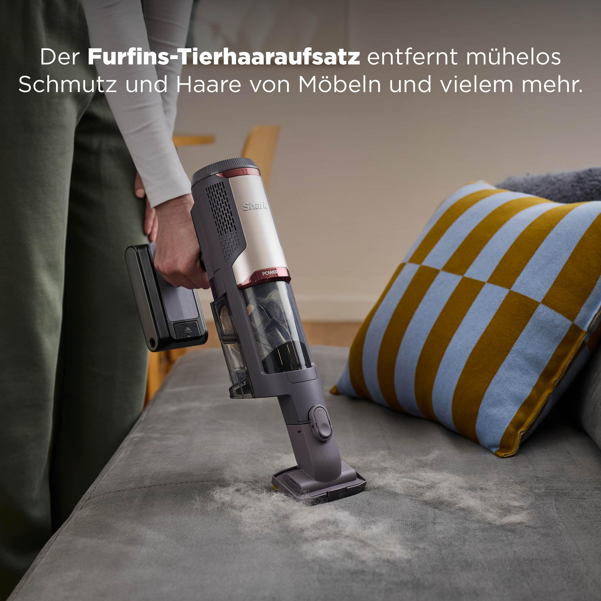 Ein Handstaubsauger reinigt eine graue Couch von Tierhaaren.