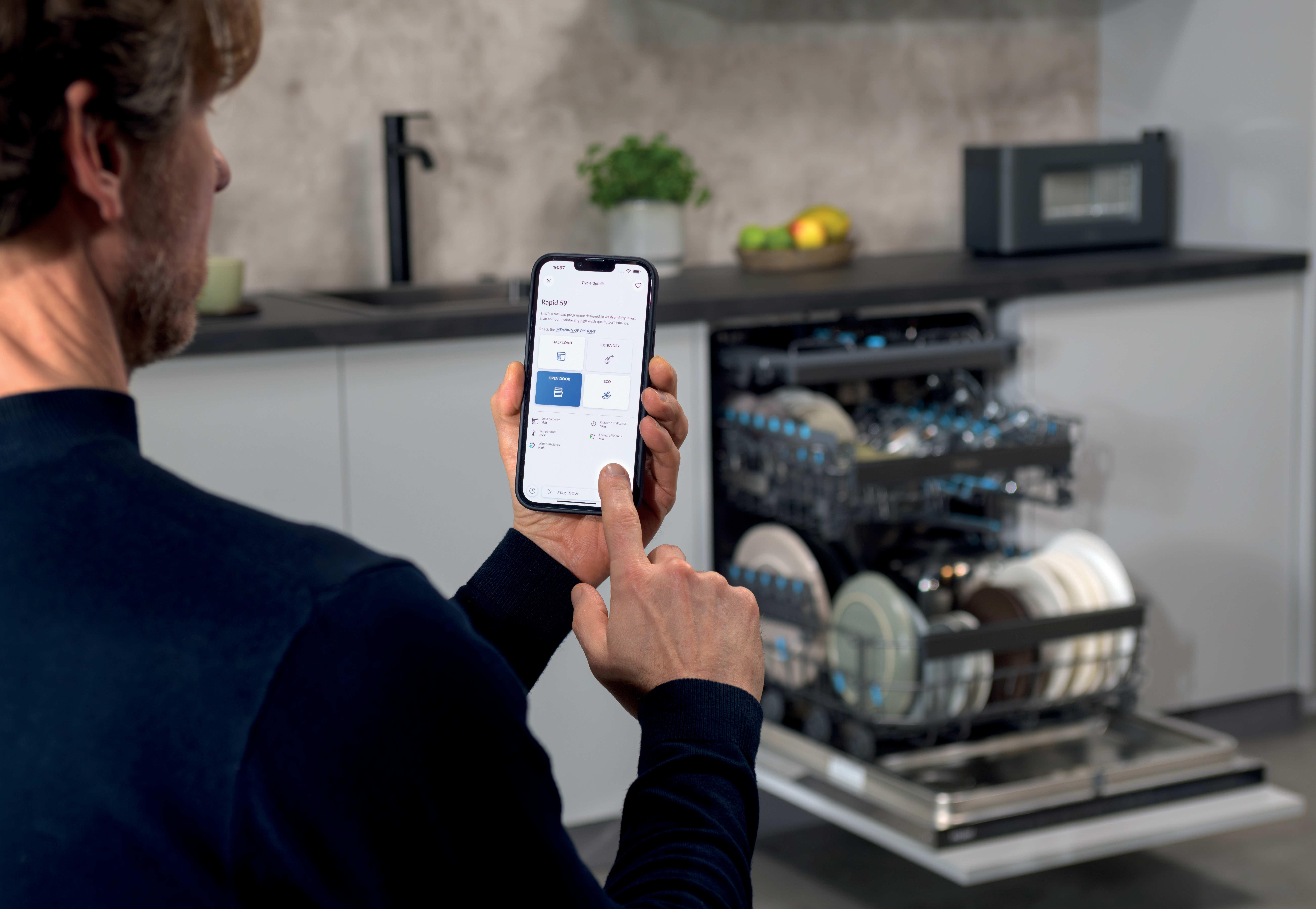 Mann bedient Spülmaschine mit Smartphone in moderner Küche.