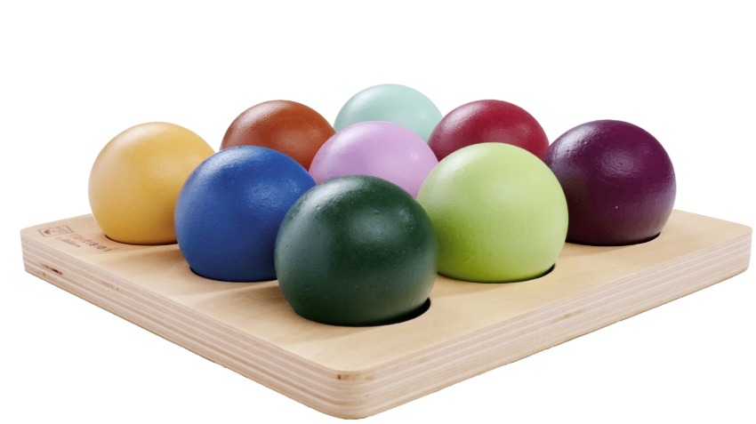 Neun bunte Holzkugeln in einer Holzform auf einem Brett.