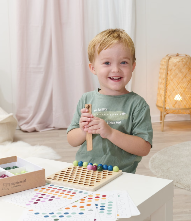 Ein Junge spielt mit einem Montessori-Zählspiel auf einem Tisch mit bunten Kugeln.