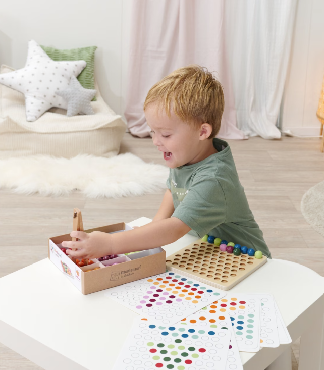 Ein Junge spielt mit Montessori-Perlen und einem Brettspiel auf einem weißen Tisch.