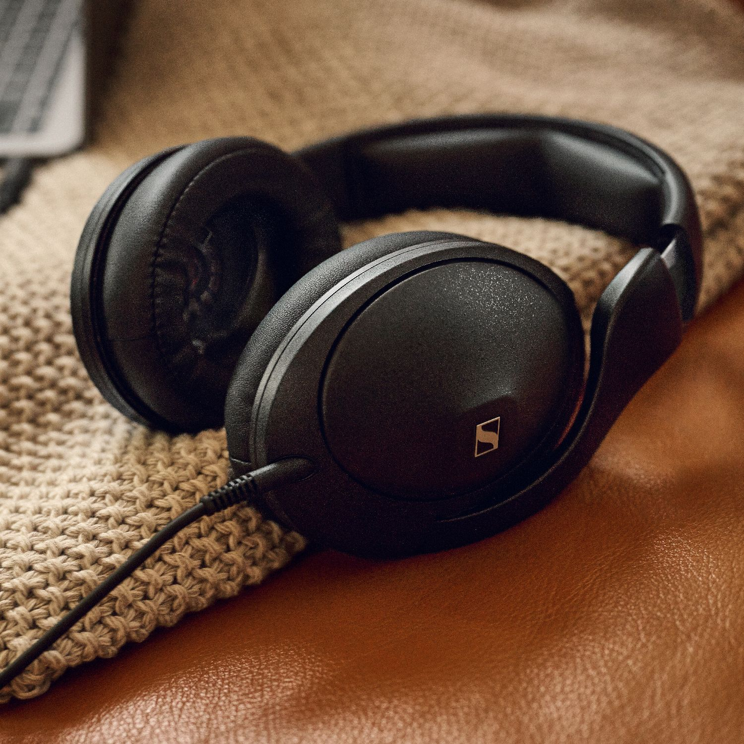 Dokulu battaniye ve kahverengi deri yüzey üzerinde siyah Sennheiser kulaklık.