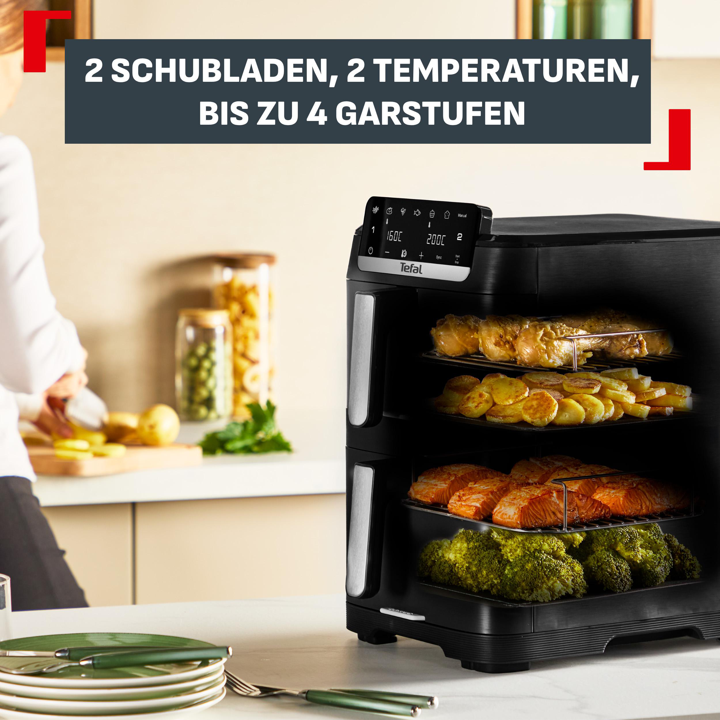Ein schwarzes Tefal Heißluftfritteusengerät mit zwei Schubladen, gefüllt mit Hühnchen, Kartoffeln, Lachs und Brokkoli.