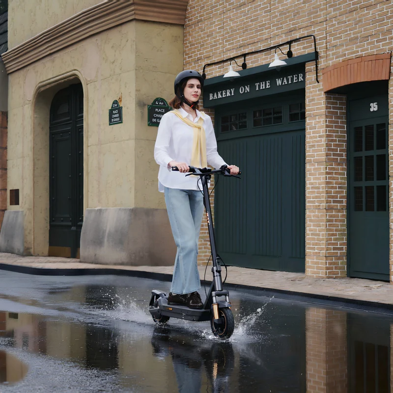 Eine Frau fährt mit einem Elektroroller durch Pfützen auf einer Straße.