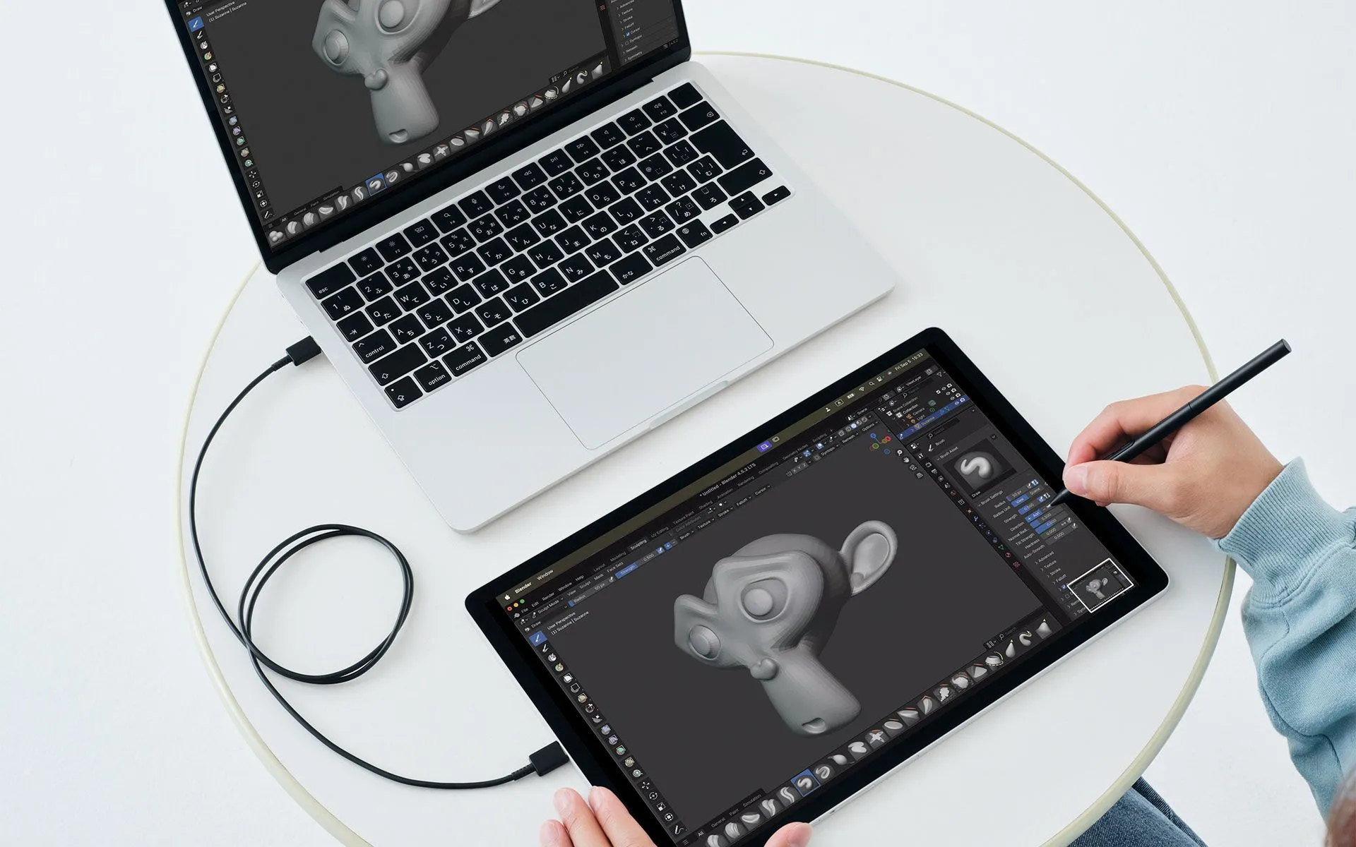 Egy laptop és egy tablet 3D modellező szoftvert jelenít meg, egy kéz érintőceruzával a tableten.