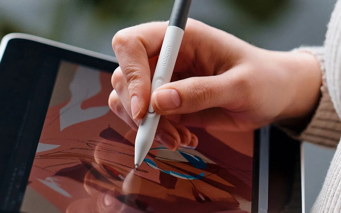 Egy kéz fehér Wacom tollat használ egy táblagépen, digitális illusztrációt rajzolva.