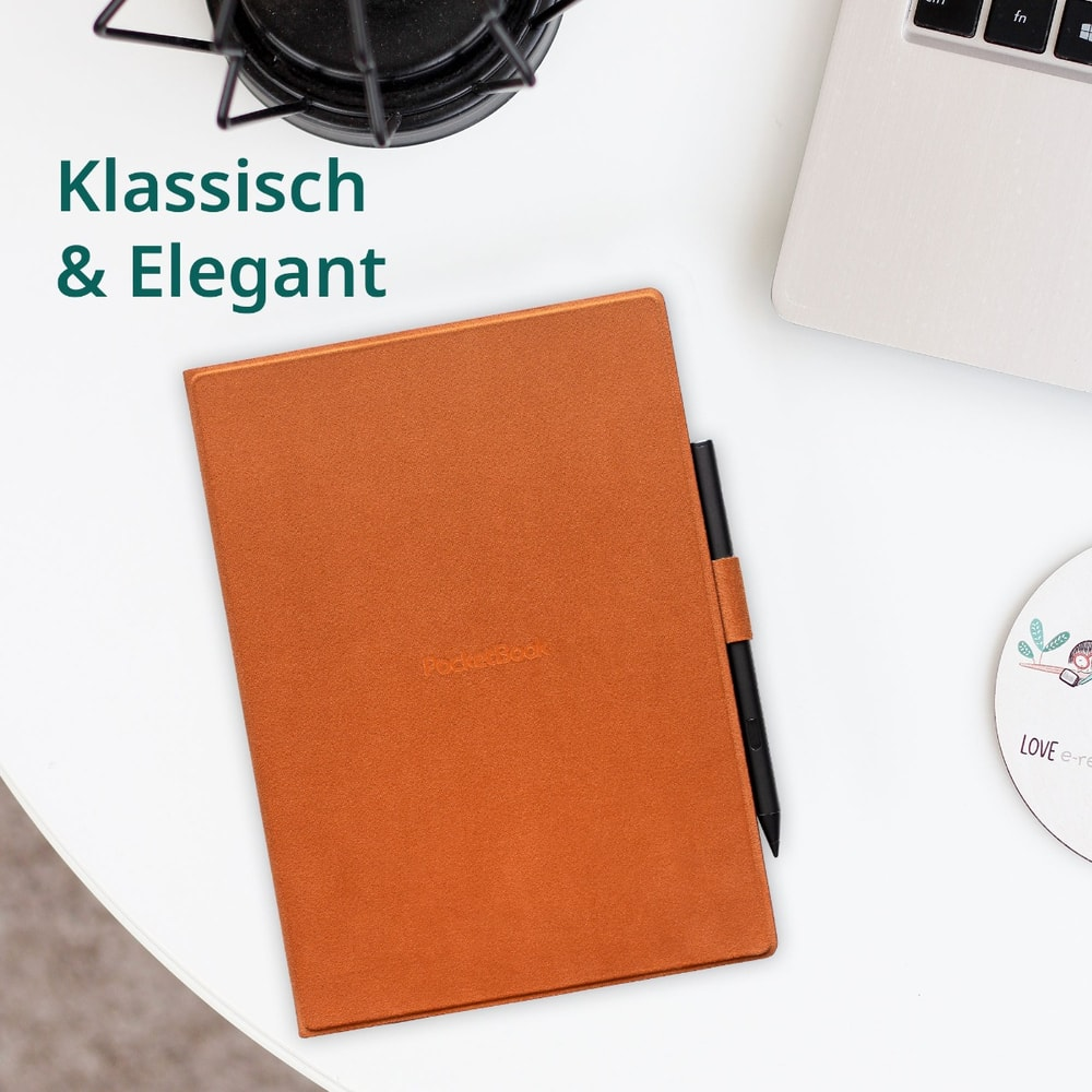 Ein braunes E-Book im Etui mit Stift, daneben ein Laptop und ein Notizbuch.