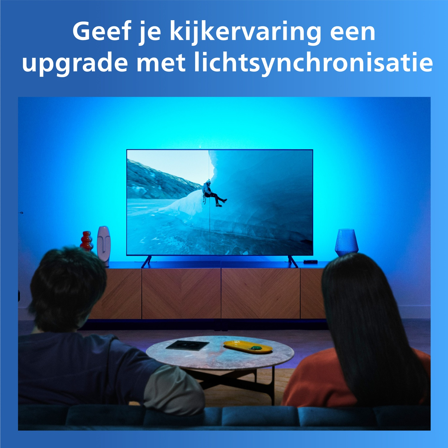 Two people sit on a couch watching a TV with blue ambient lighting behind it.