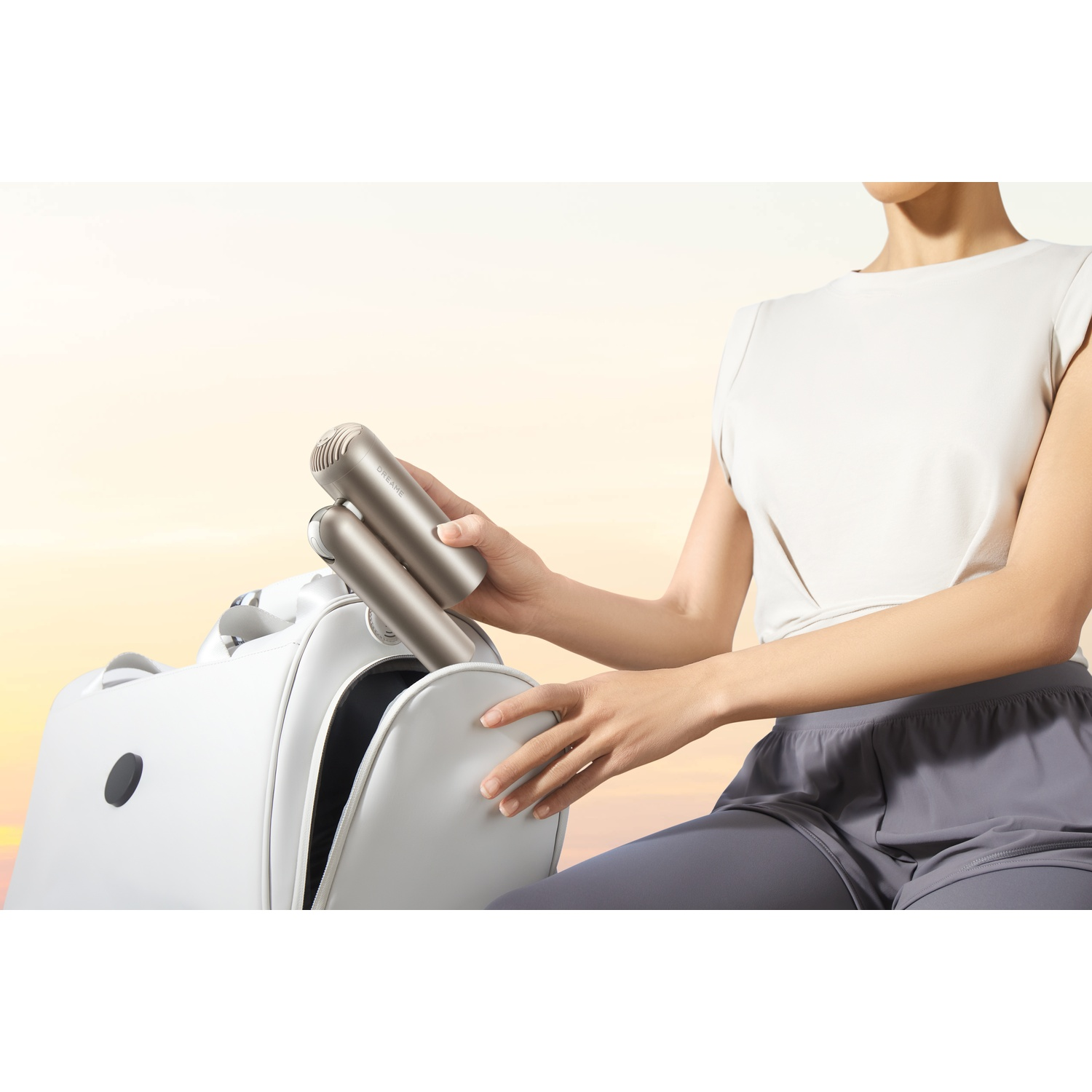A person places a silver massage gun into a white bag at sunset.