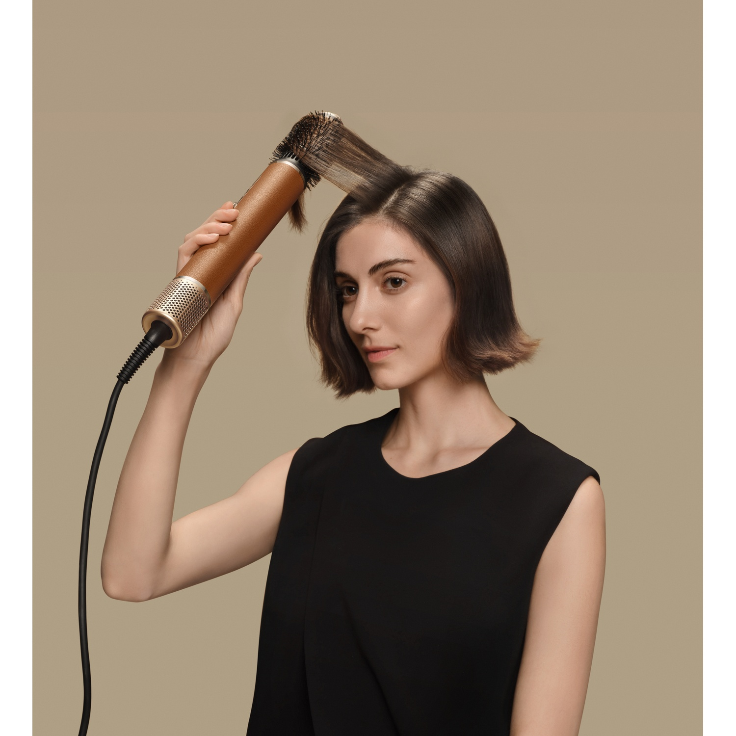 Vrouw met kort bruin haar stylet haar met een gouden föhnborstel.
