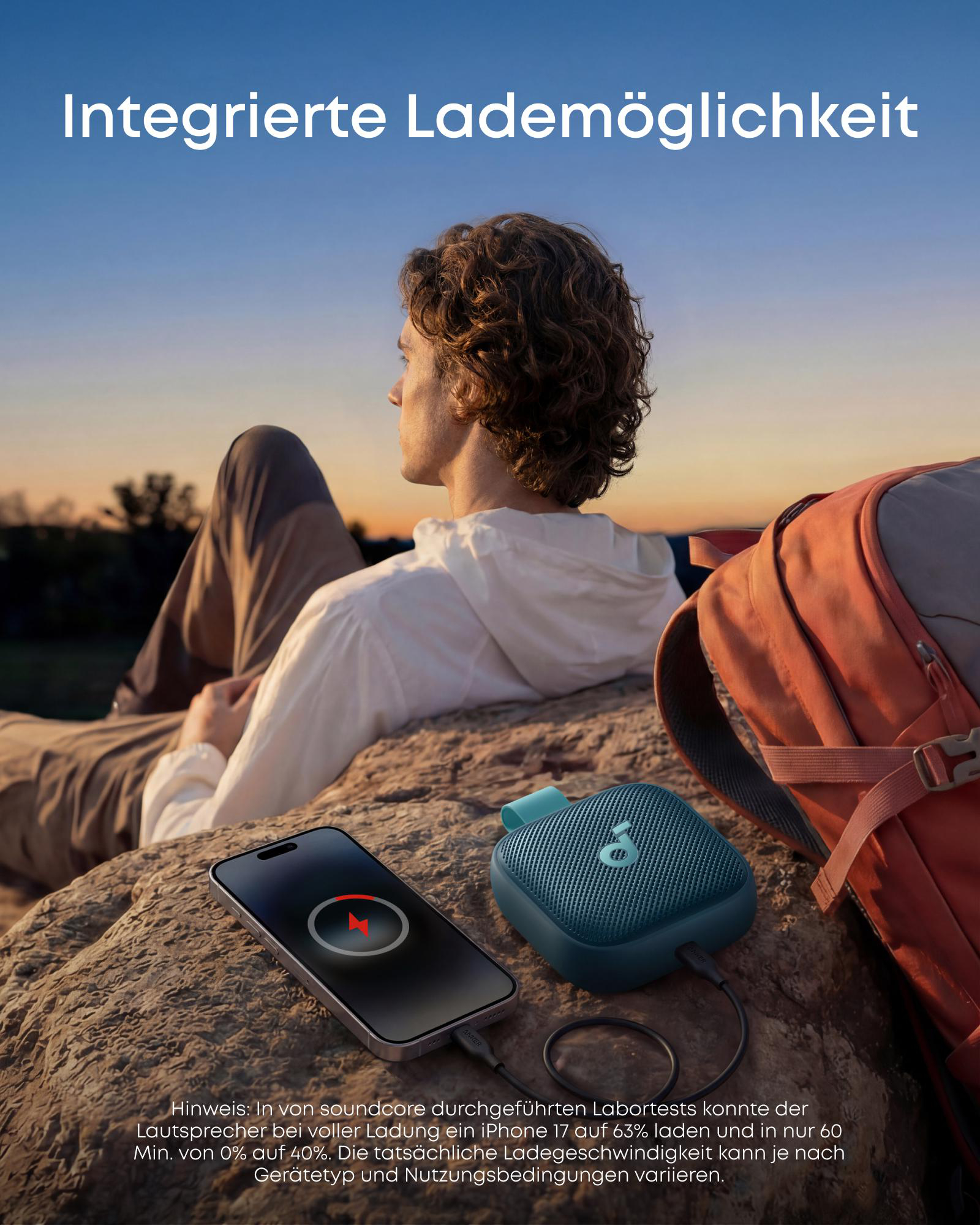 Mann sitzt draußen, lädt ein Smartphone mit Bluetooth-Lautsprecher. Rucksack daneben.