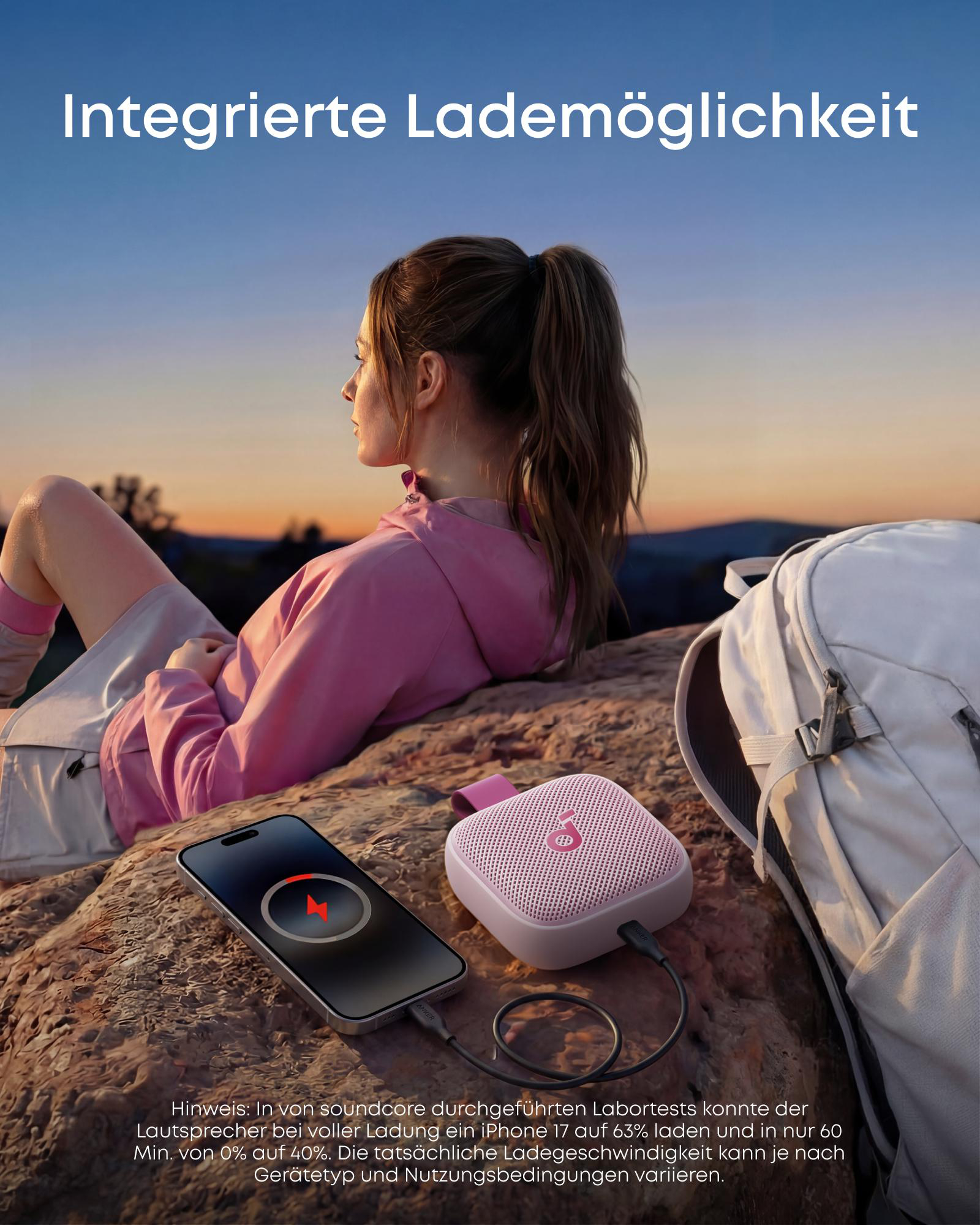 Eine Frau sitzt draußen. Ein Handy lädt über einen Lautsprecher. Ein Rucksack liegt daneben.