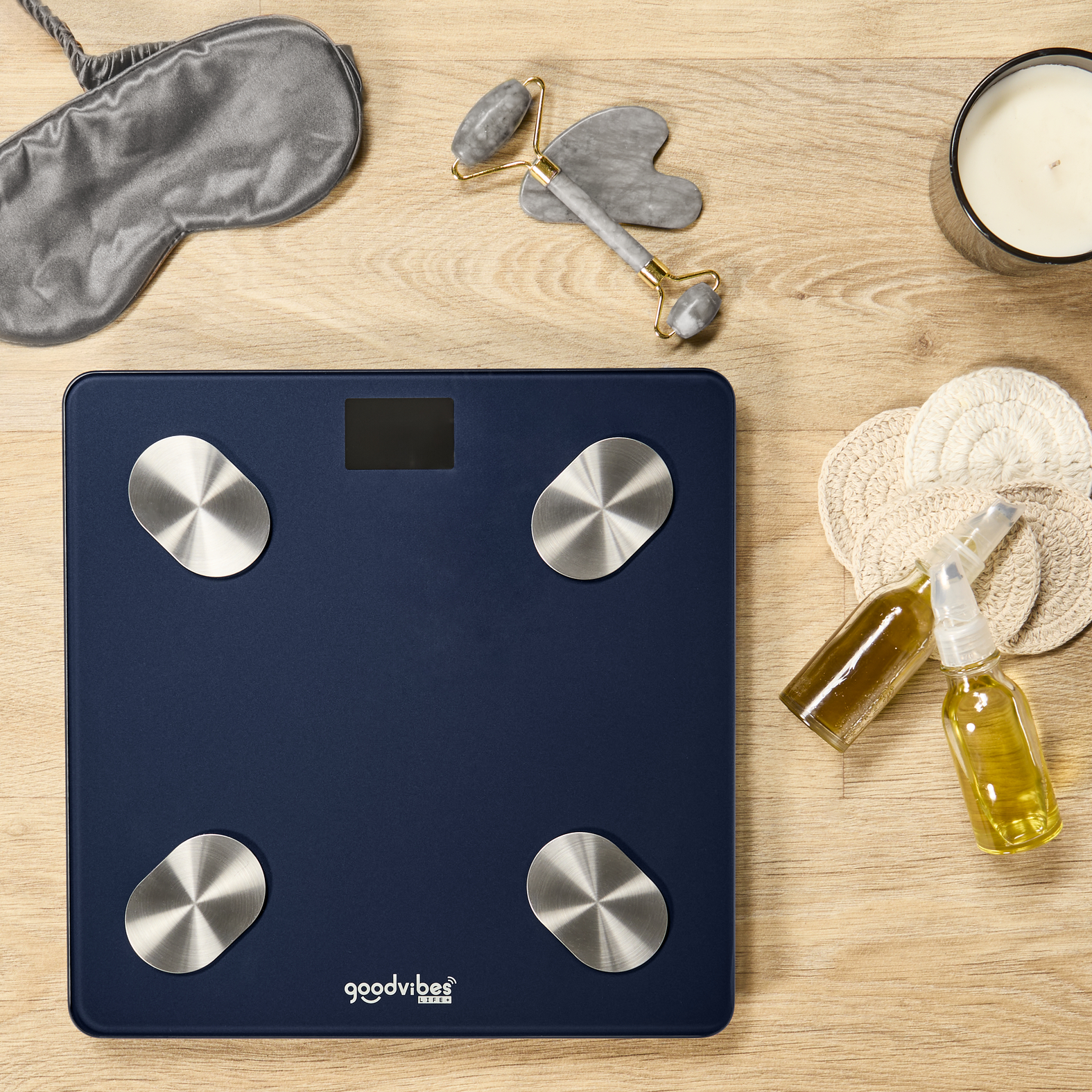 Balanza azul oscuro con sensores plateados, al lado una máscara de dormir, rodillo facial y vela.