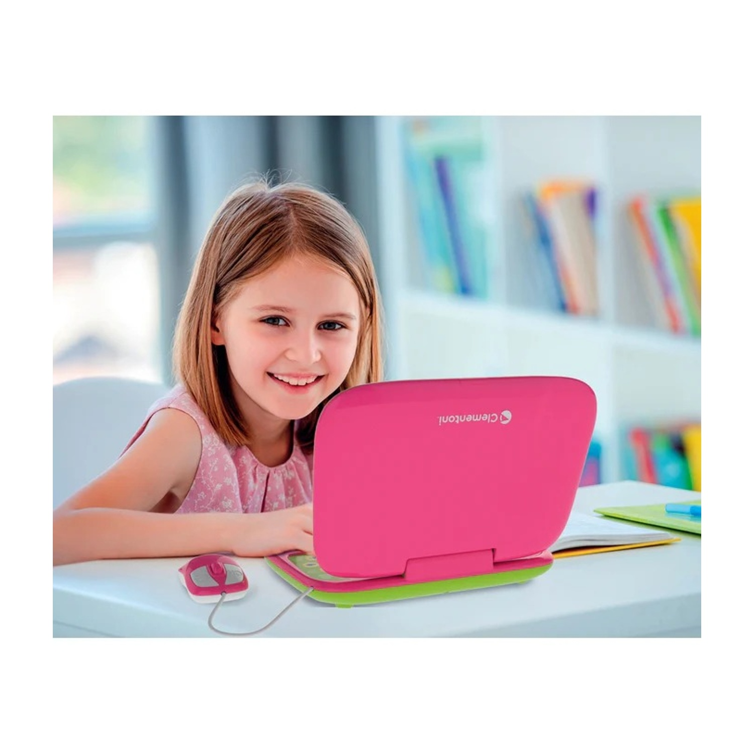 Una ragazza sorride mentre usa un laptop rosa e verde con un mouse su una scrivania.