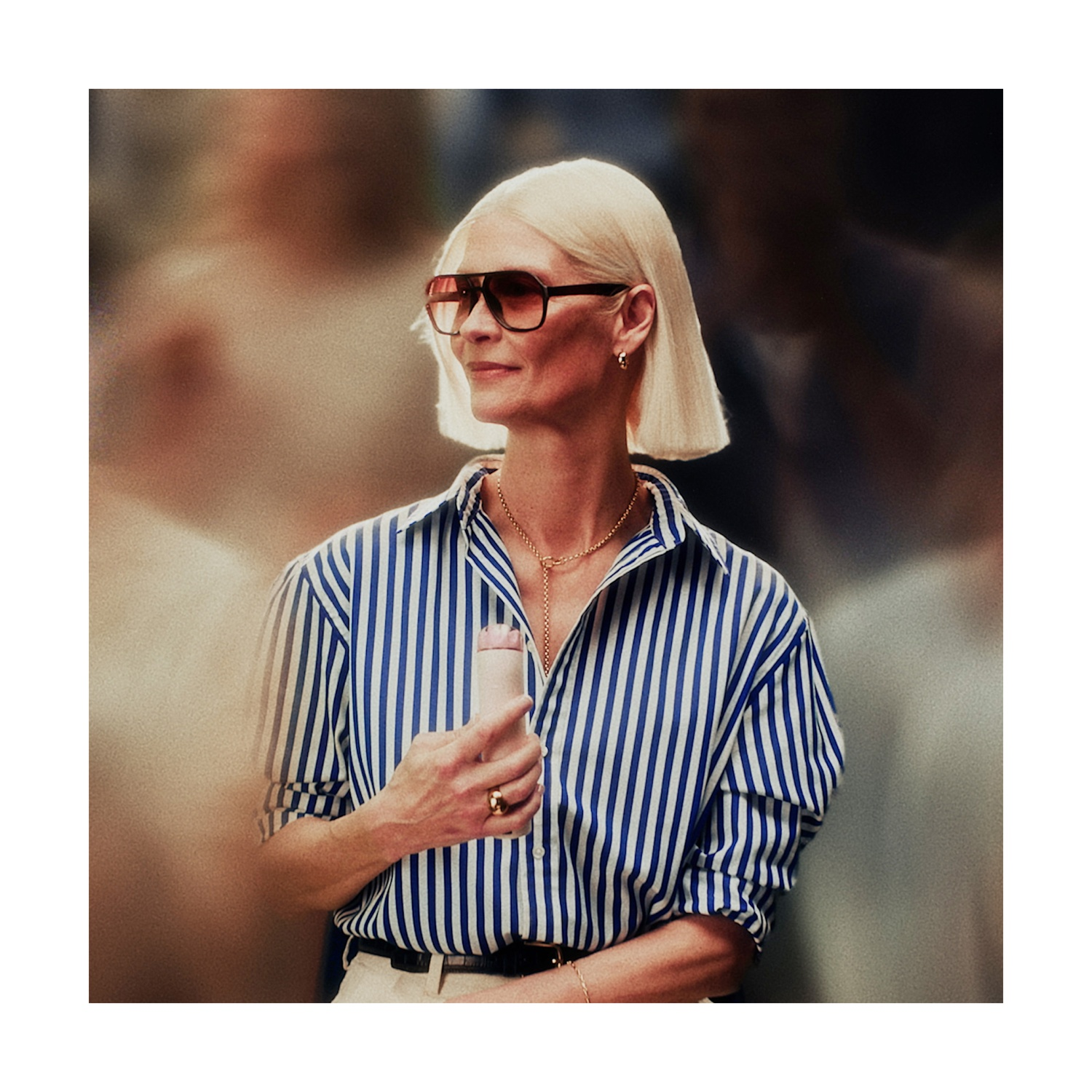 Donna con capelli biondi, occhiali da sole, camicia a righe blu e bianche tiene un piccolo rotolo bianco.