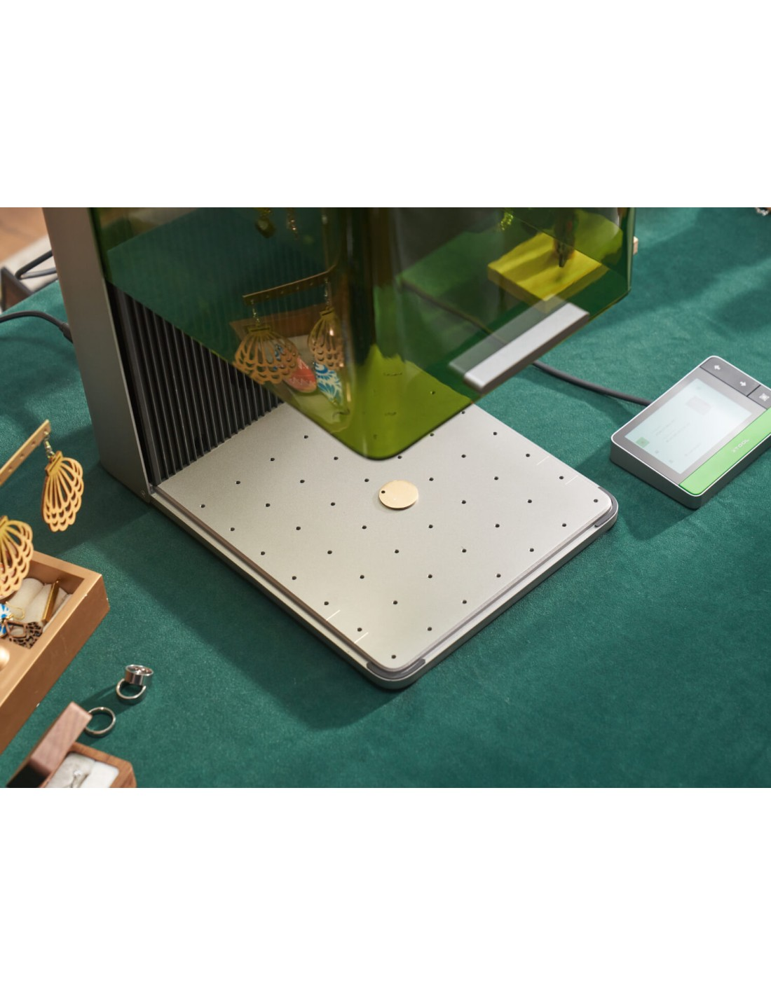 Un grabador láser con joyas sobre una superficie verde. Un disco dorado está sobre la plataforma.