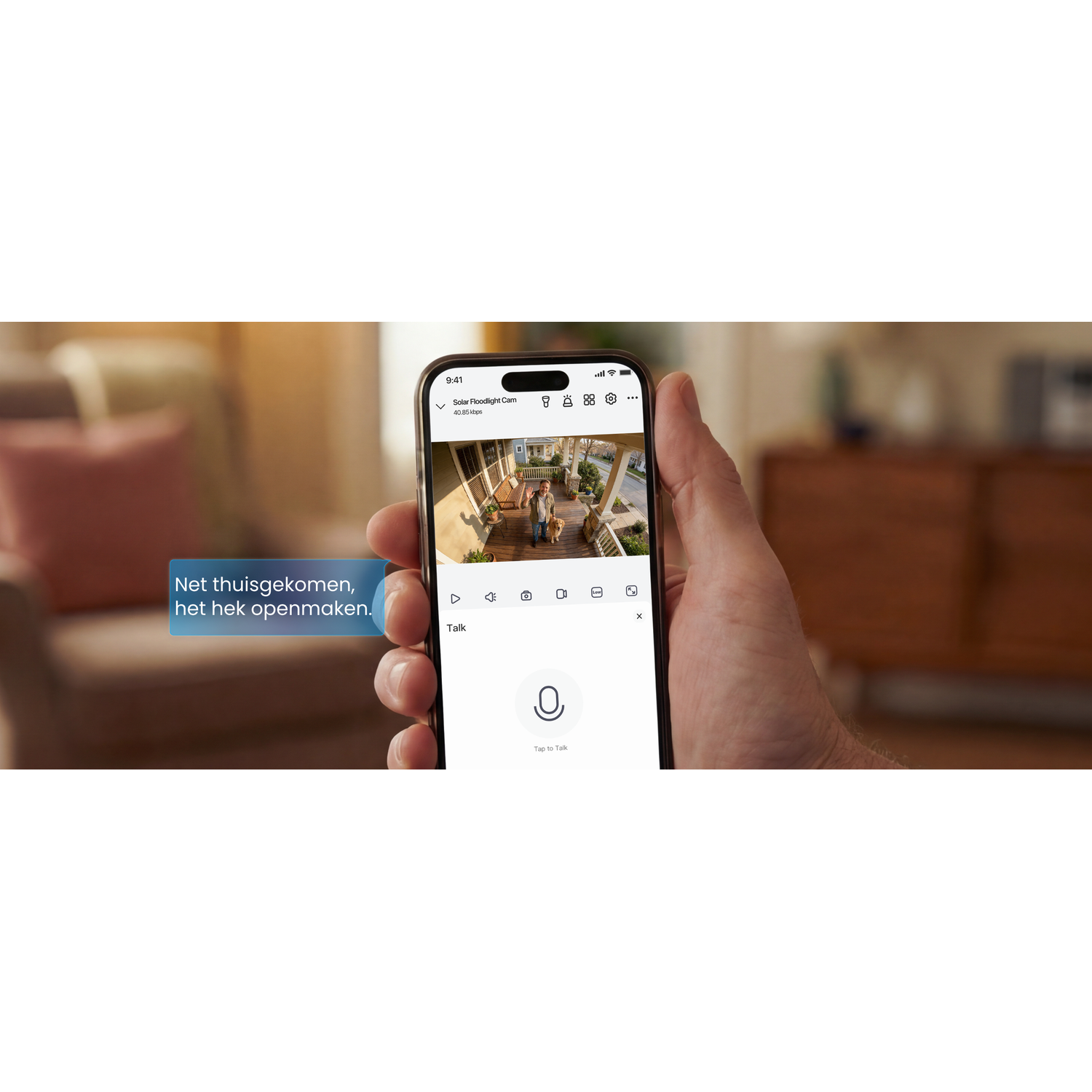 A person holds a phone displaying a security camera app. A dog and a person are visible on screen.