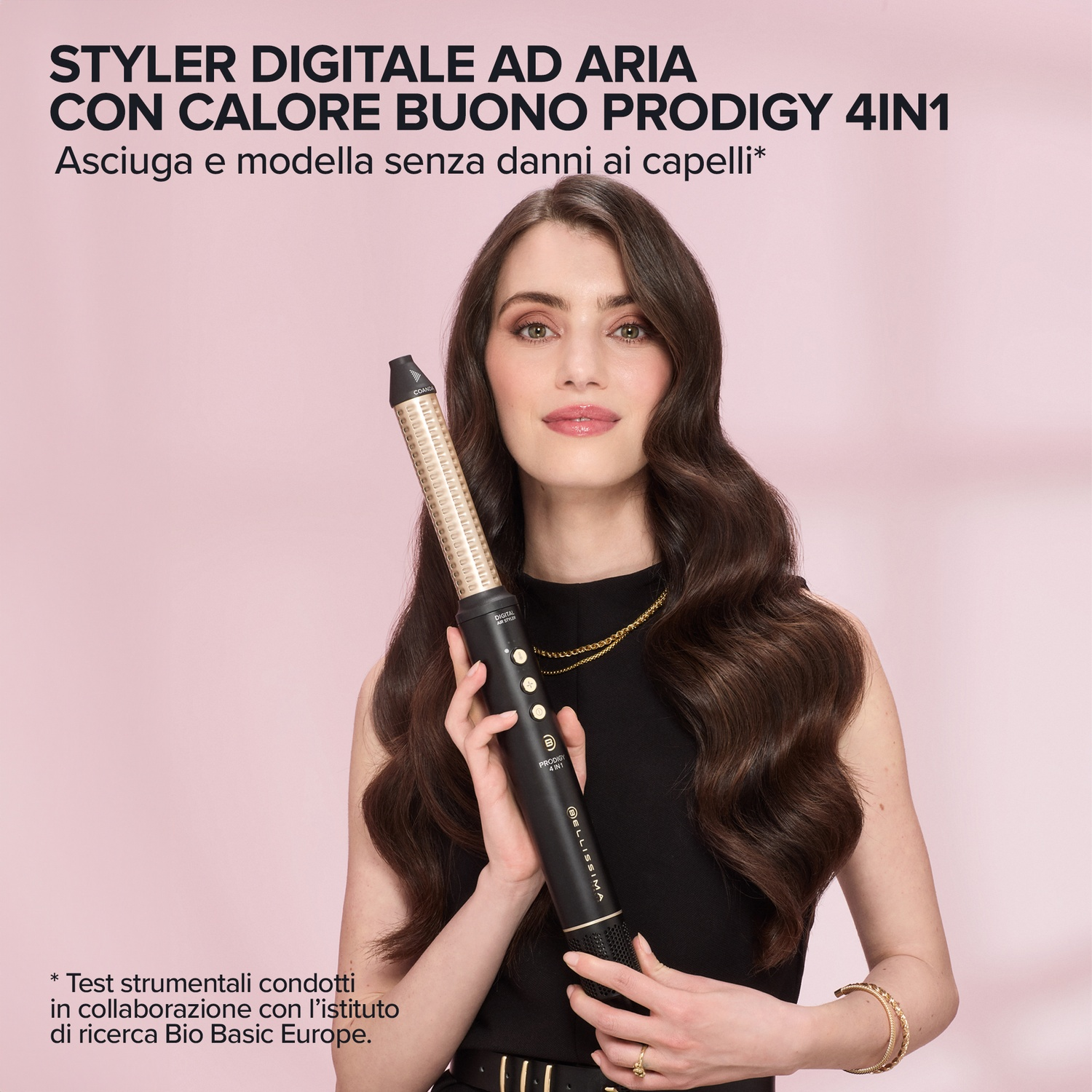 Una donna tiene uno styler asciugacapelli nero con accenti dorati su sfondo rosa.