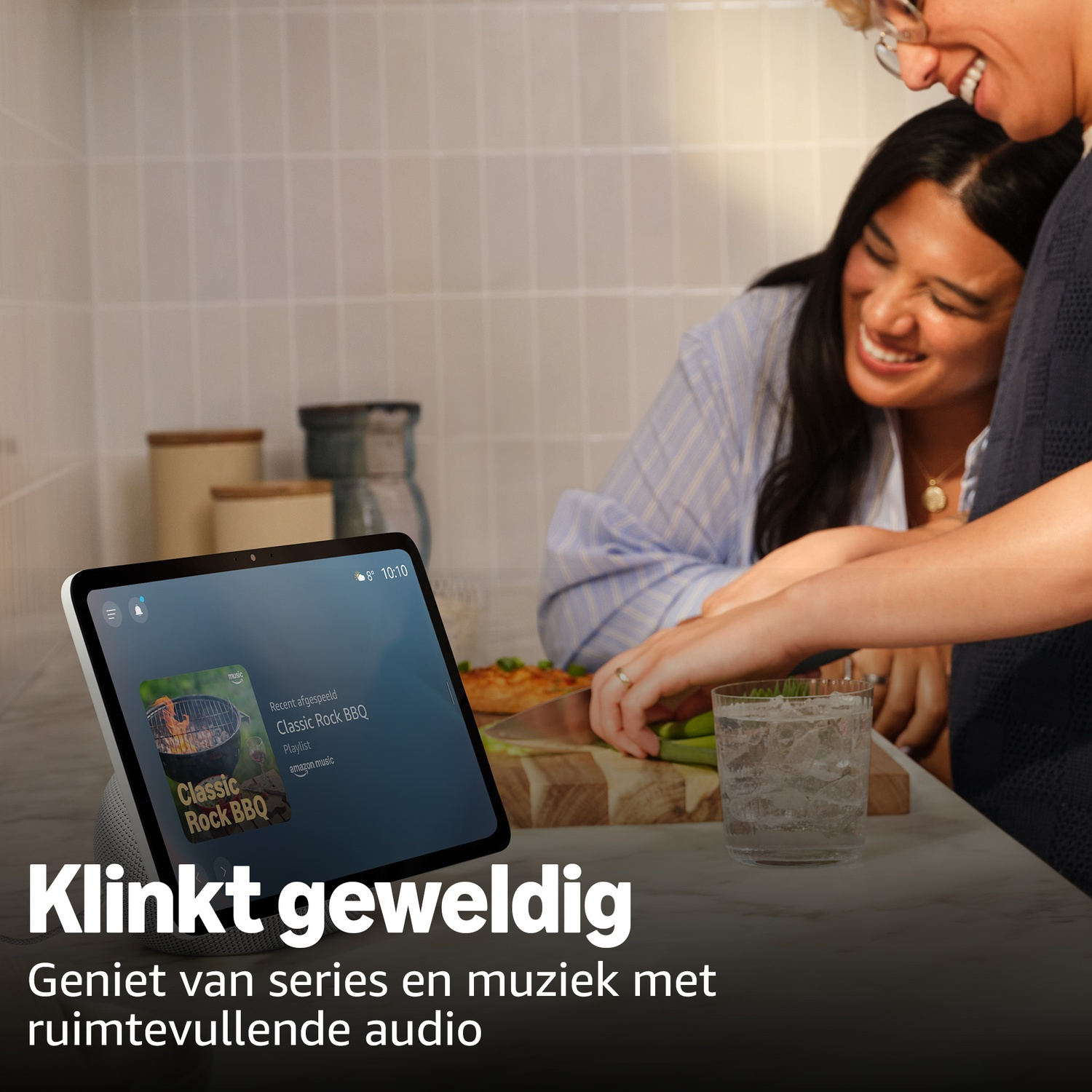 Twee mensen in een keuken, één kijkt naar een smart display met muziek.