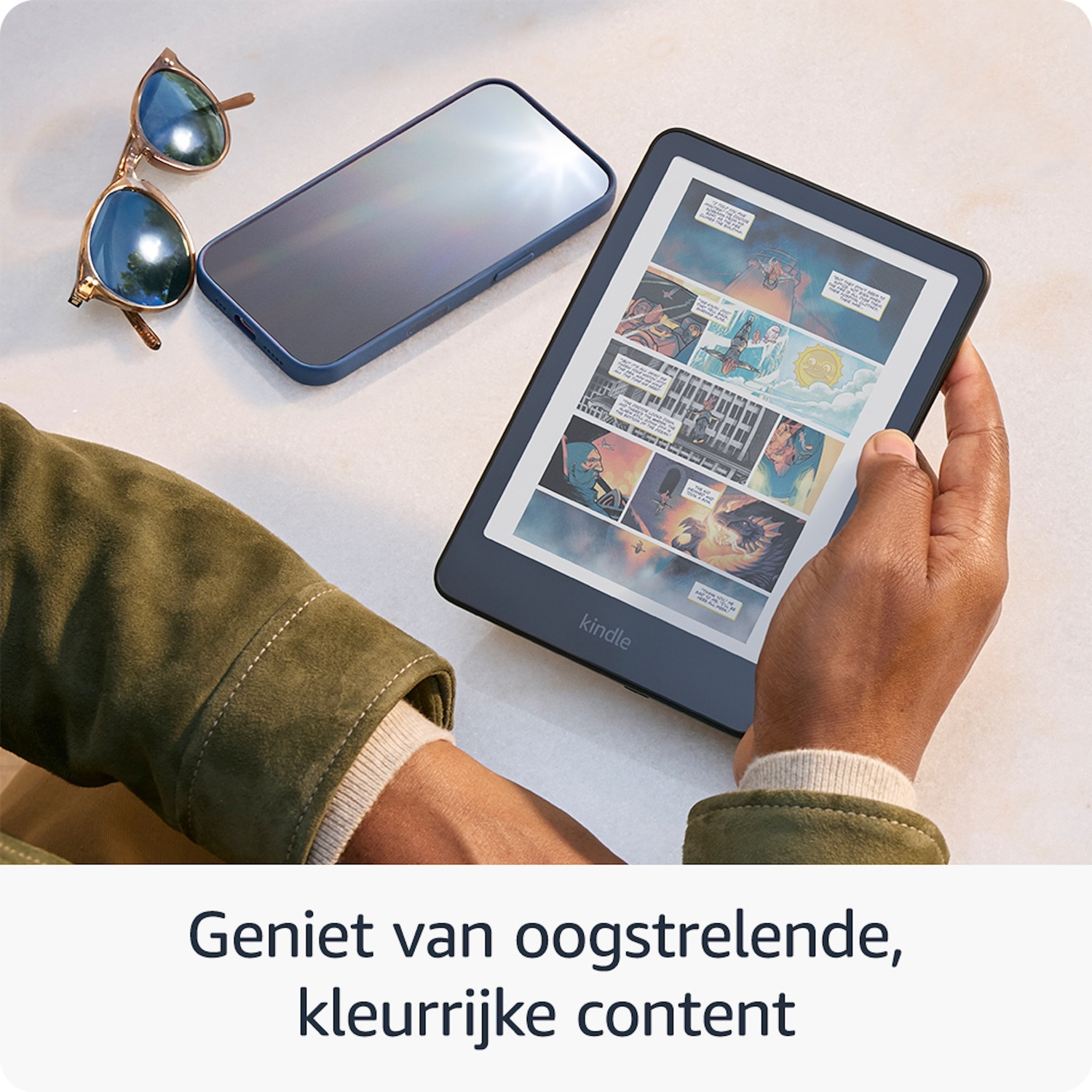 Een hand houdt een Kindle vast, ernaast een zonnebril en smartphone.