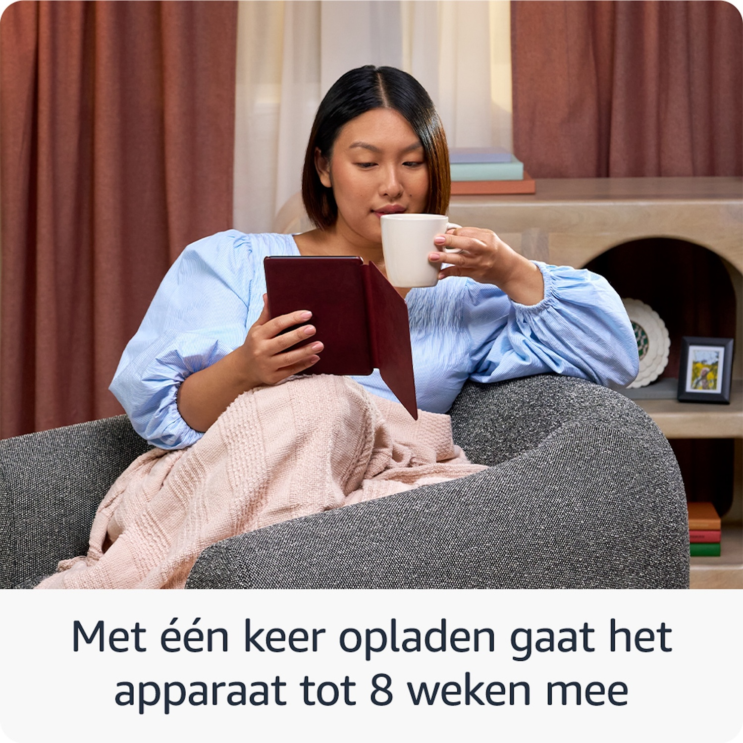 Een vrouw zit in een stoel, leest een boek en drinkt.