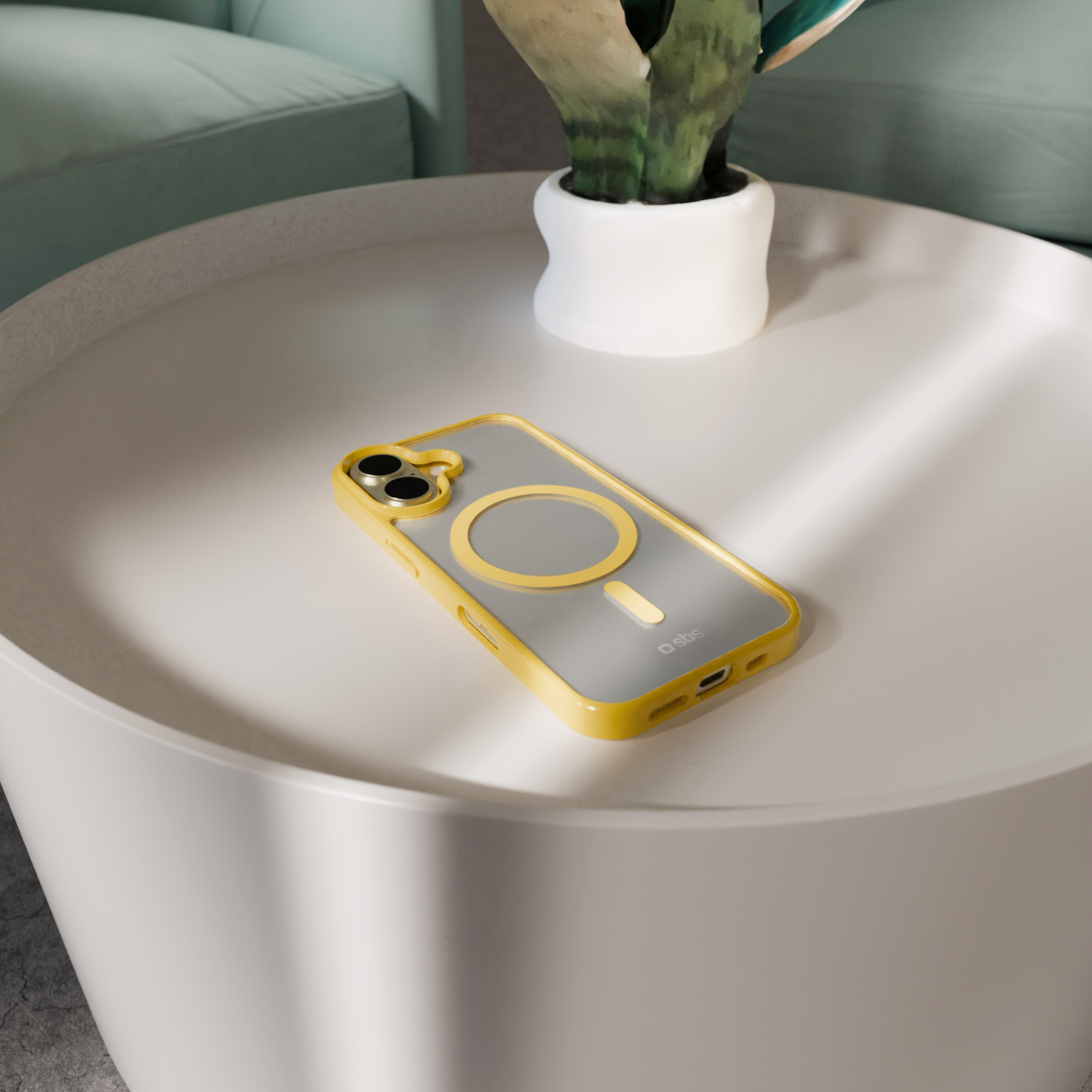 Ein gelbes iPhone-Case mit MagSafe liegt auf einem weißen Tisch neben einer Topfpflanze.
