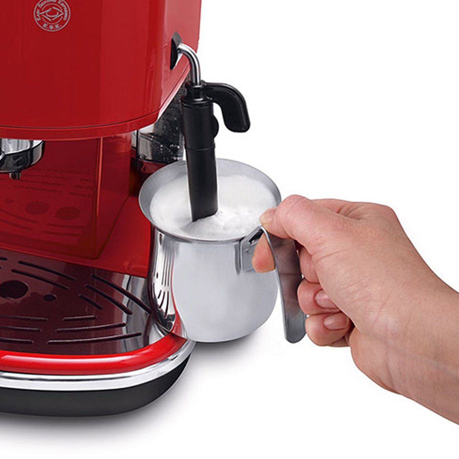 Una mano tiene una lattiera in metallo con latte montato accanto a una macchina del caffè rossa.