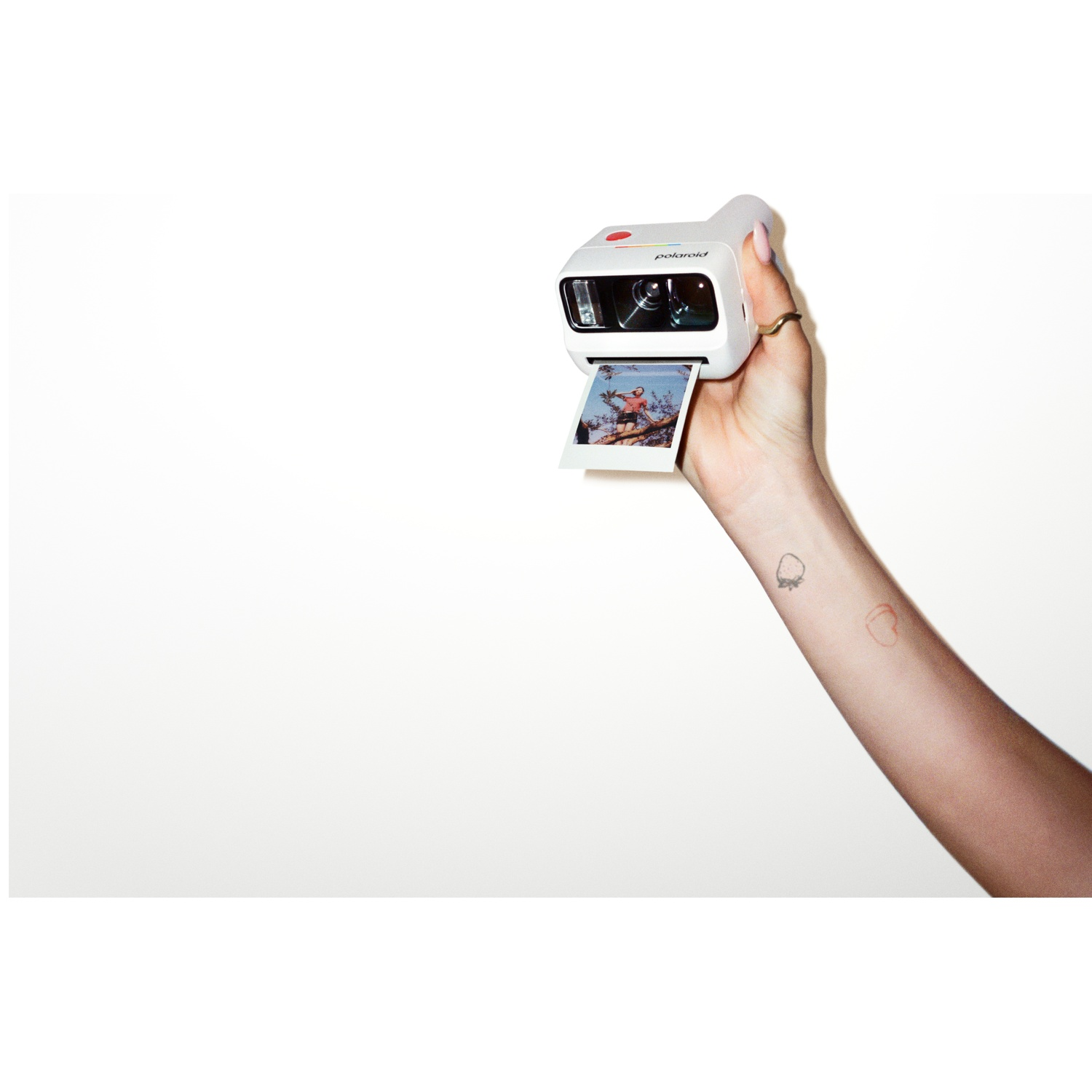 Une main tient un appareil photo Polaroid blanc avec une photo d'une femme sur un arbre.