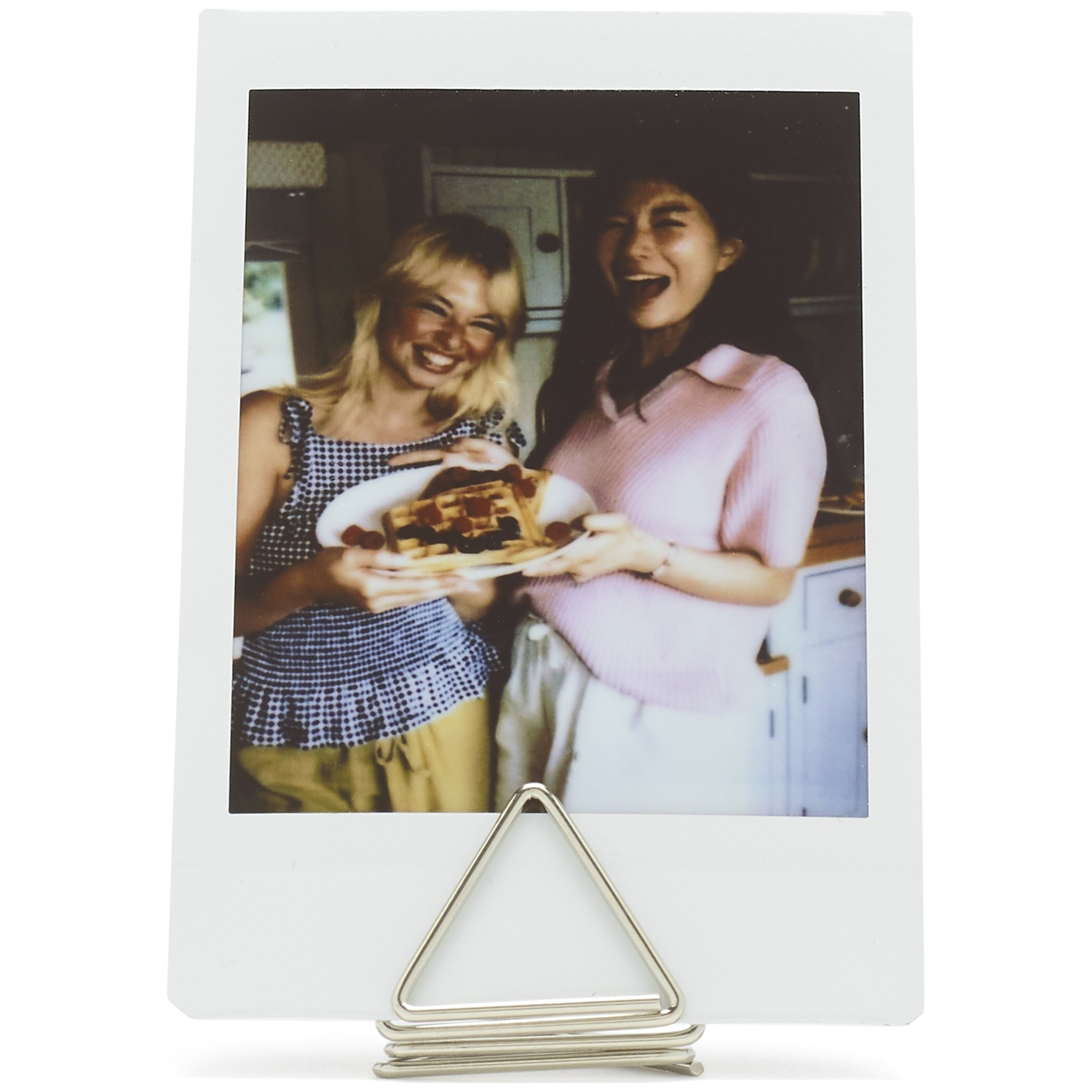 Two women laugh, one holding a plate of waffles with berries and syrup.