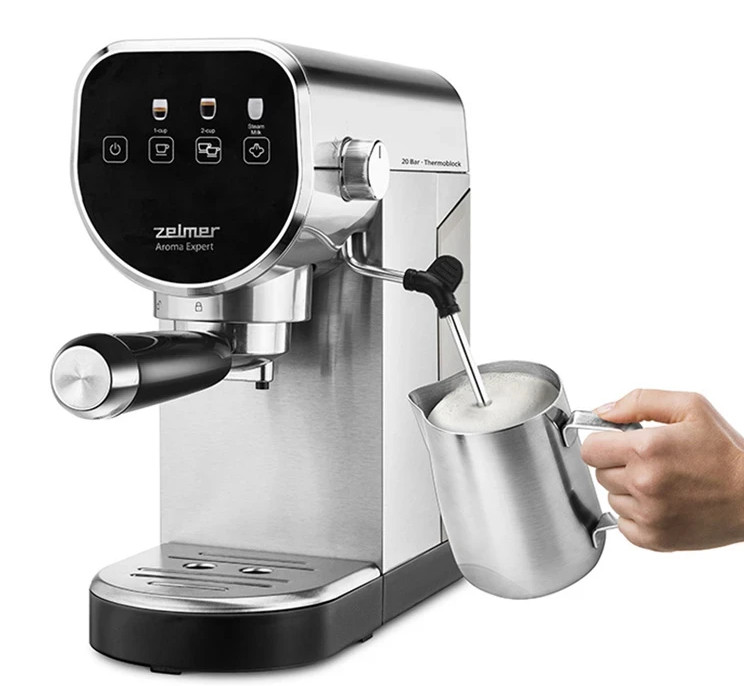 Srebrna maszyna do espresso z czarnym uchwytem spienia mleko w metalowym dzbanku.