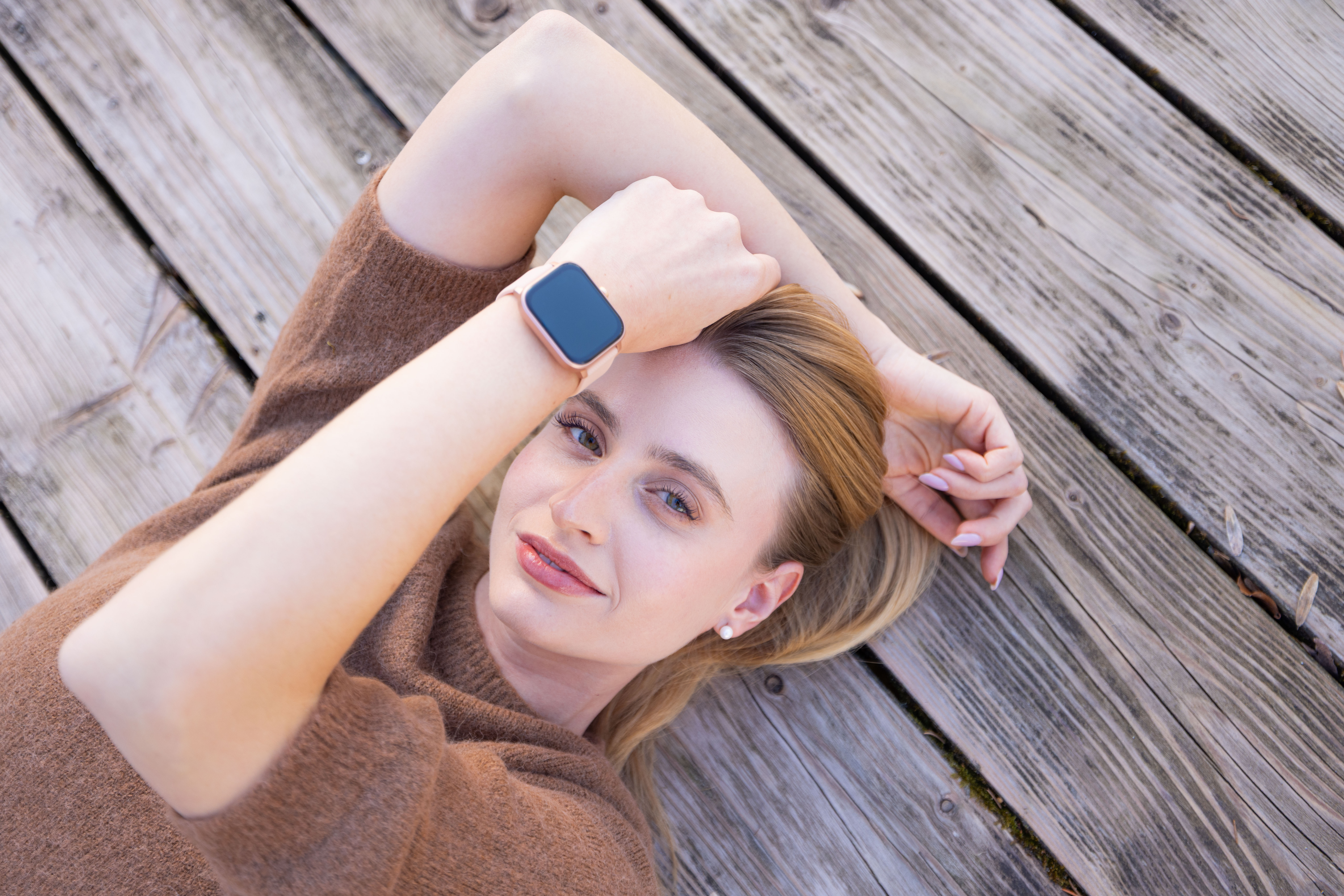 Frau mit Smartwatch liegt auf Holzplanken, Kopf auf Arm.